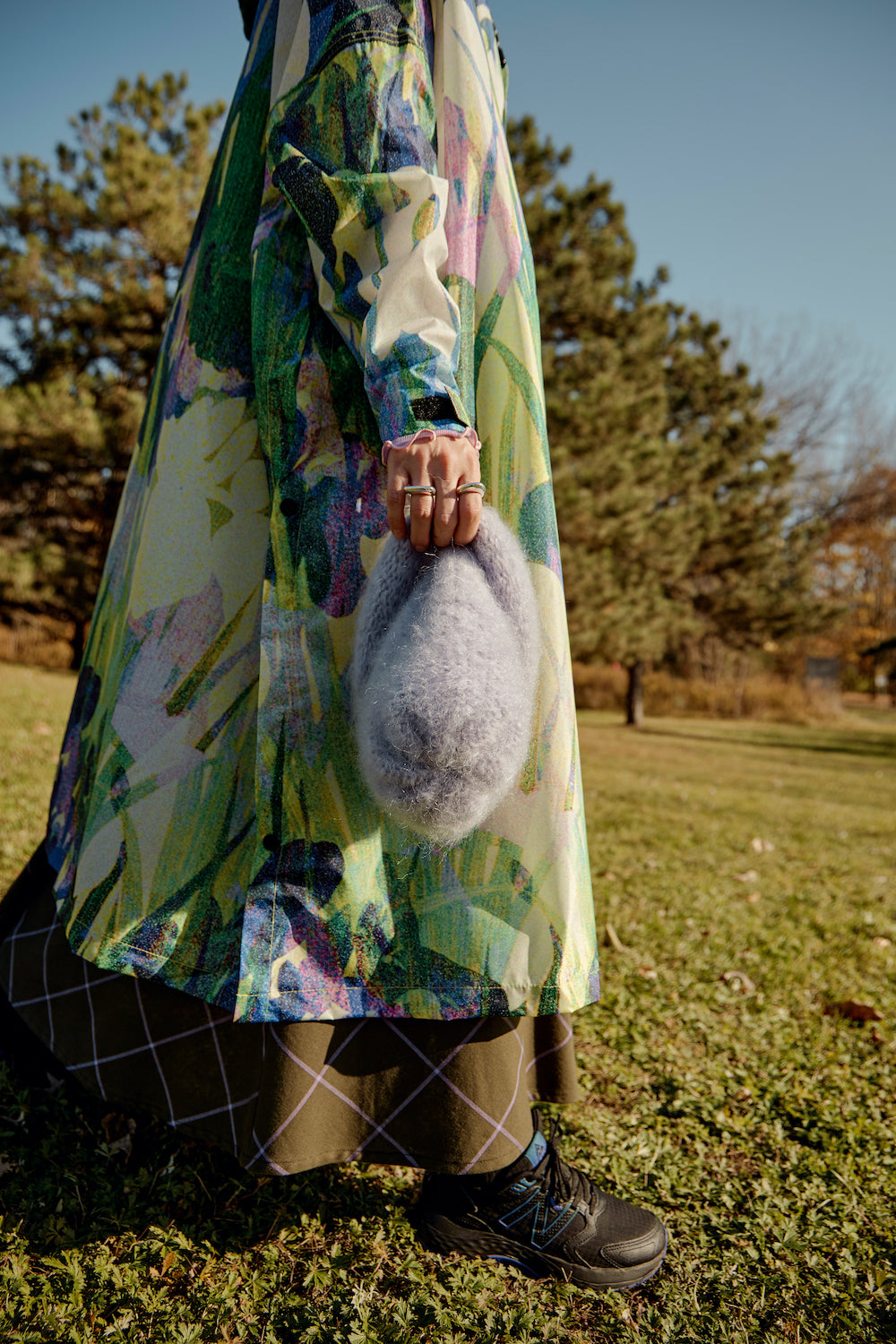 Hand adorned with rings holding a lilac mohair beanie against the fabric of a long raincoat, showcasing a stylish, cozy accessory.