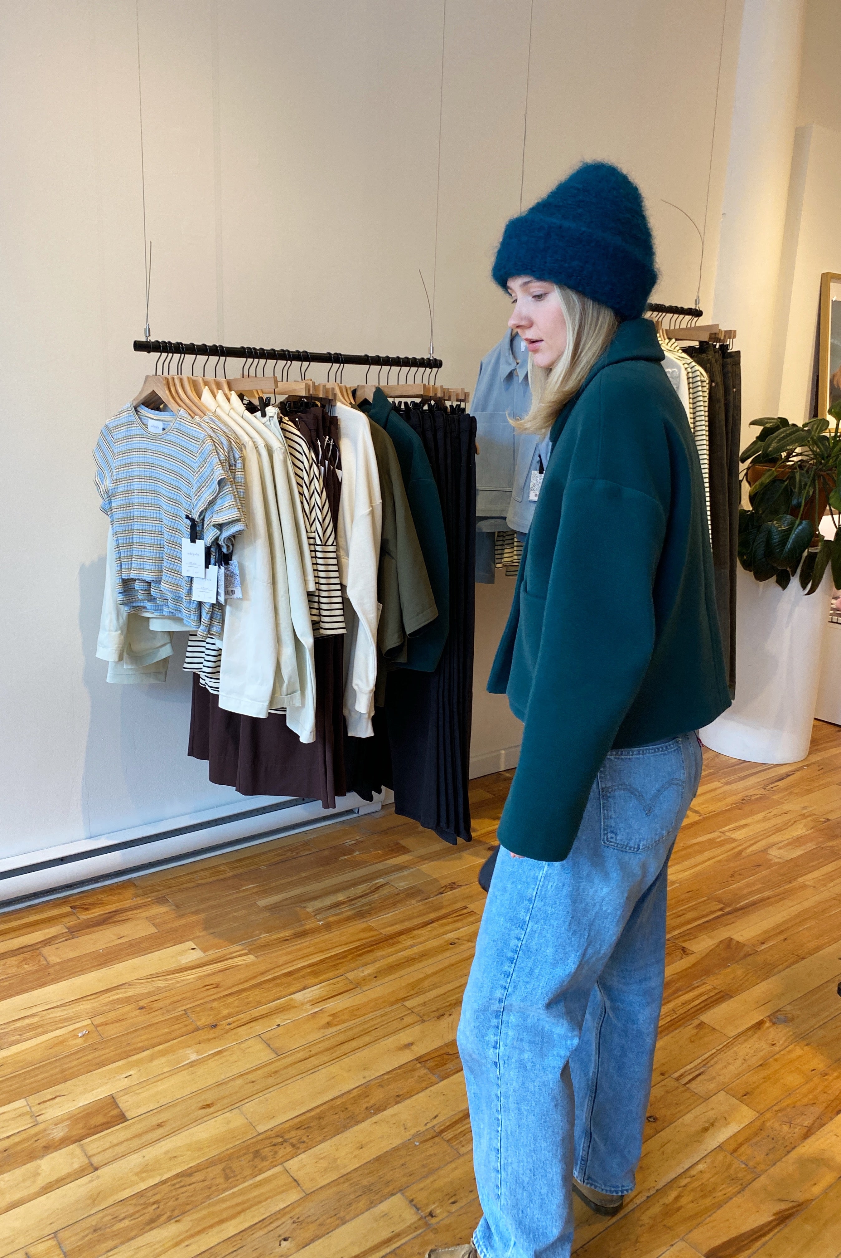A blond-haired model standing in a retail store, wearing a fuzzy green mohair beanie by Heirloom Hats.