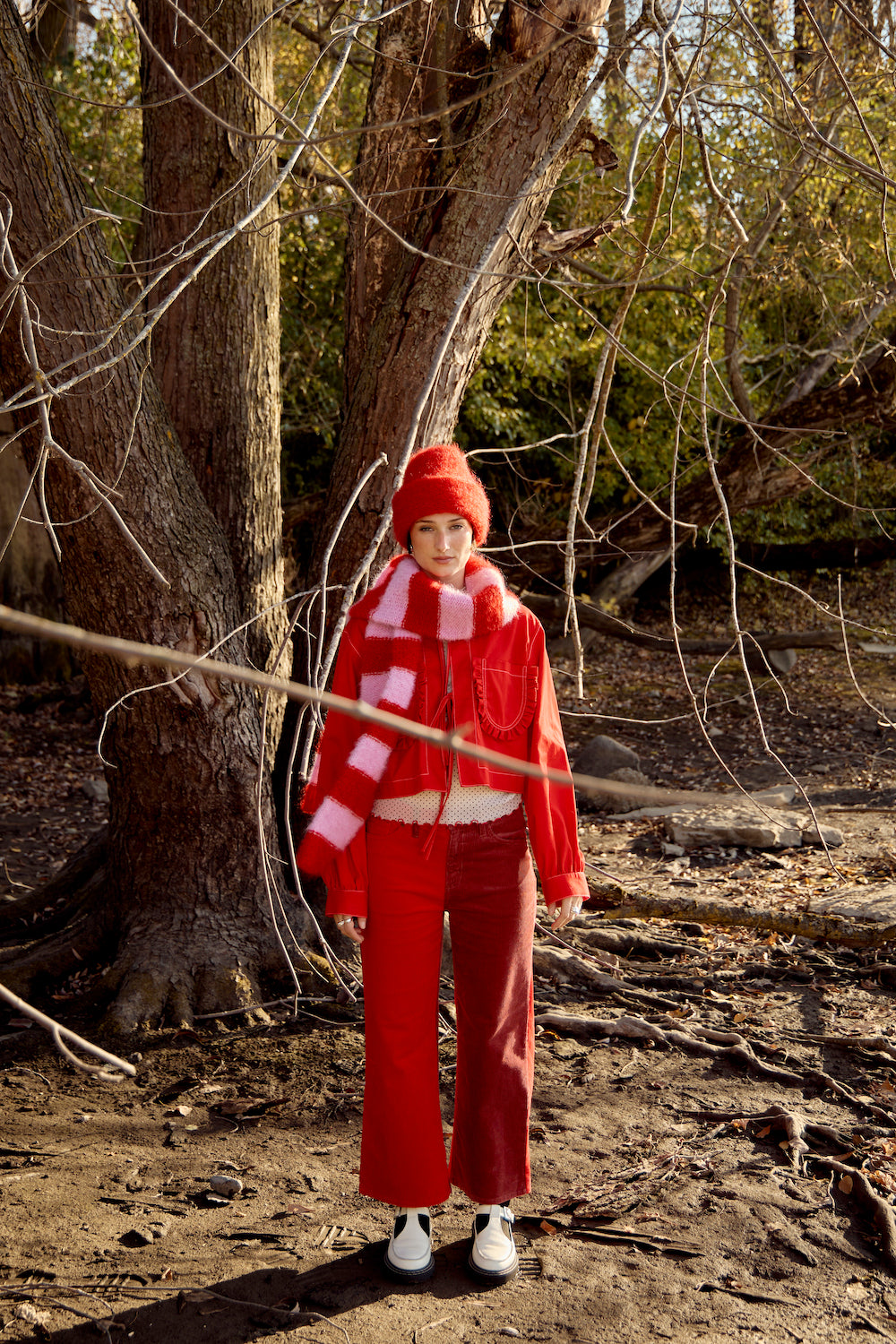 Model with a short brown bob in a red jacket, wearing a fuzzy red mohair beanie and a pink and red striped scarf by Heirloom Hats.