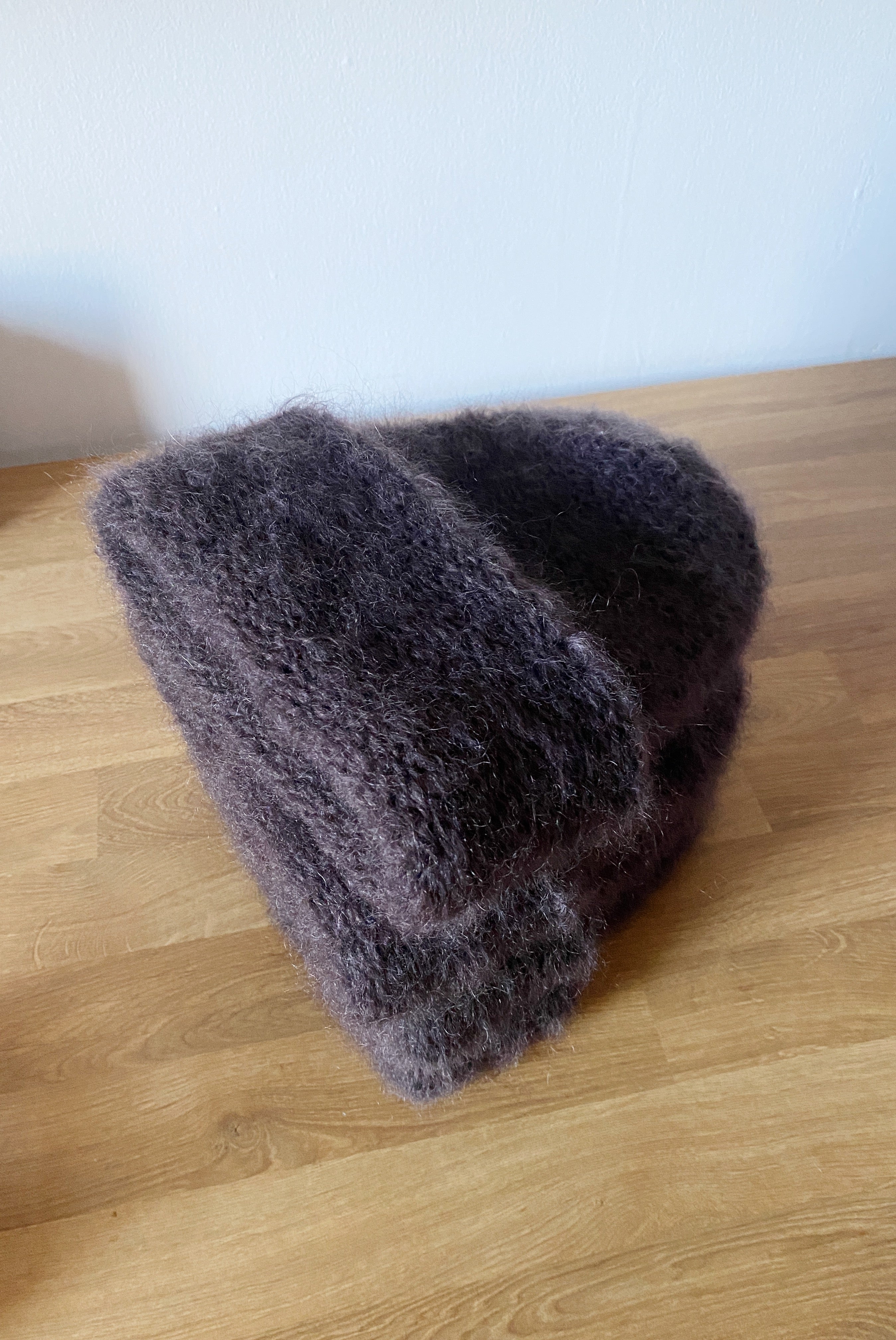 A stack of 4 chocolate mohair beanies by heirloom hats laying on a wooden counter.