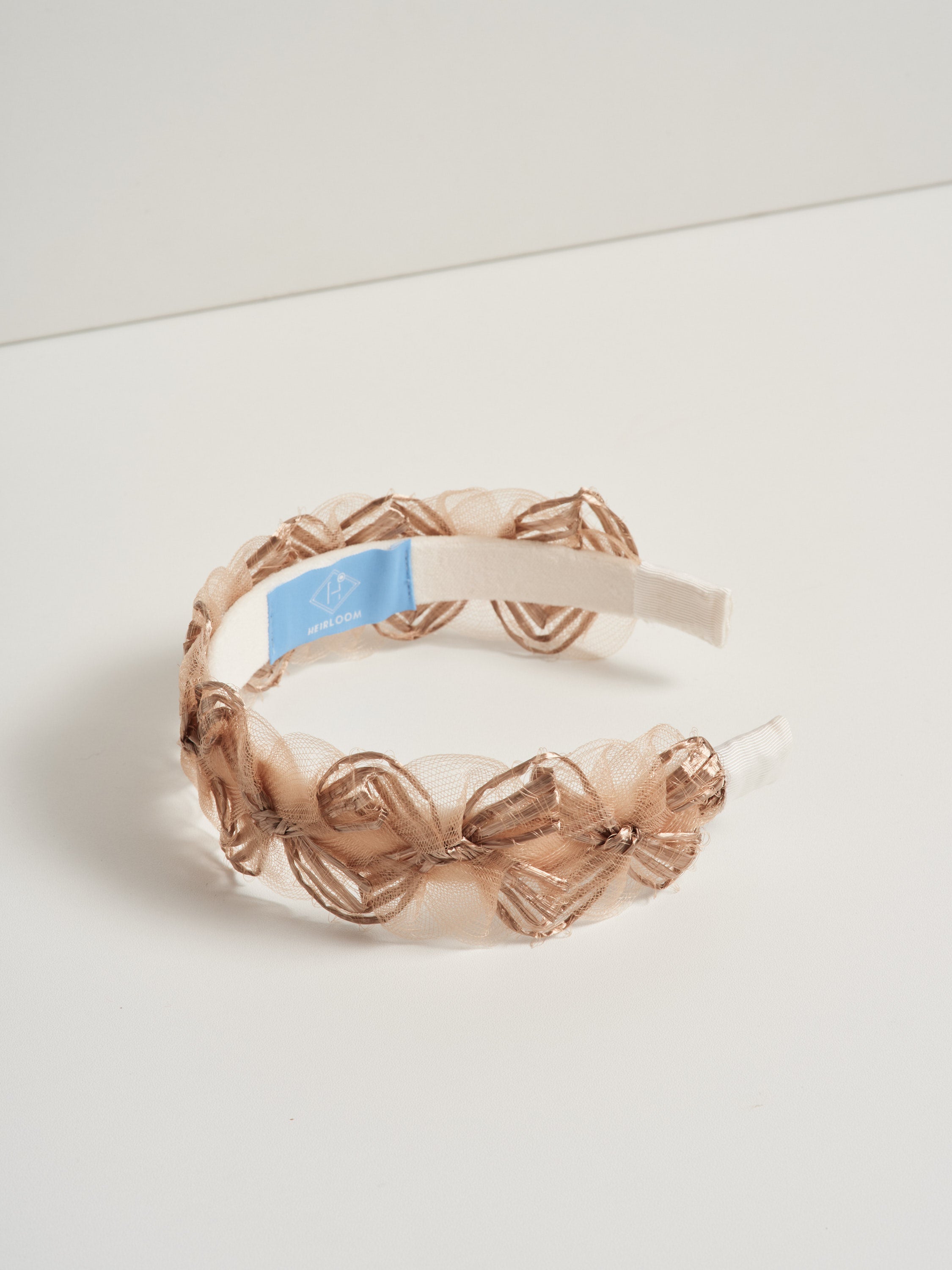 A bronze coloured headband made with deadstock straw, pictured on a white background.