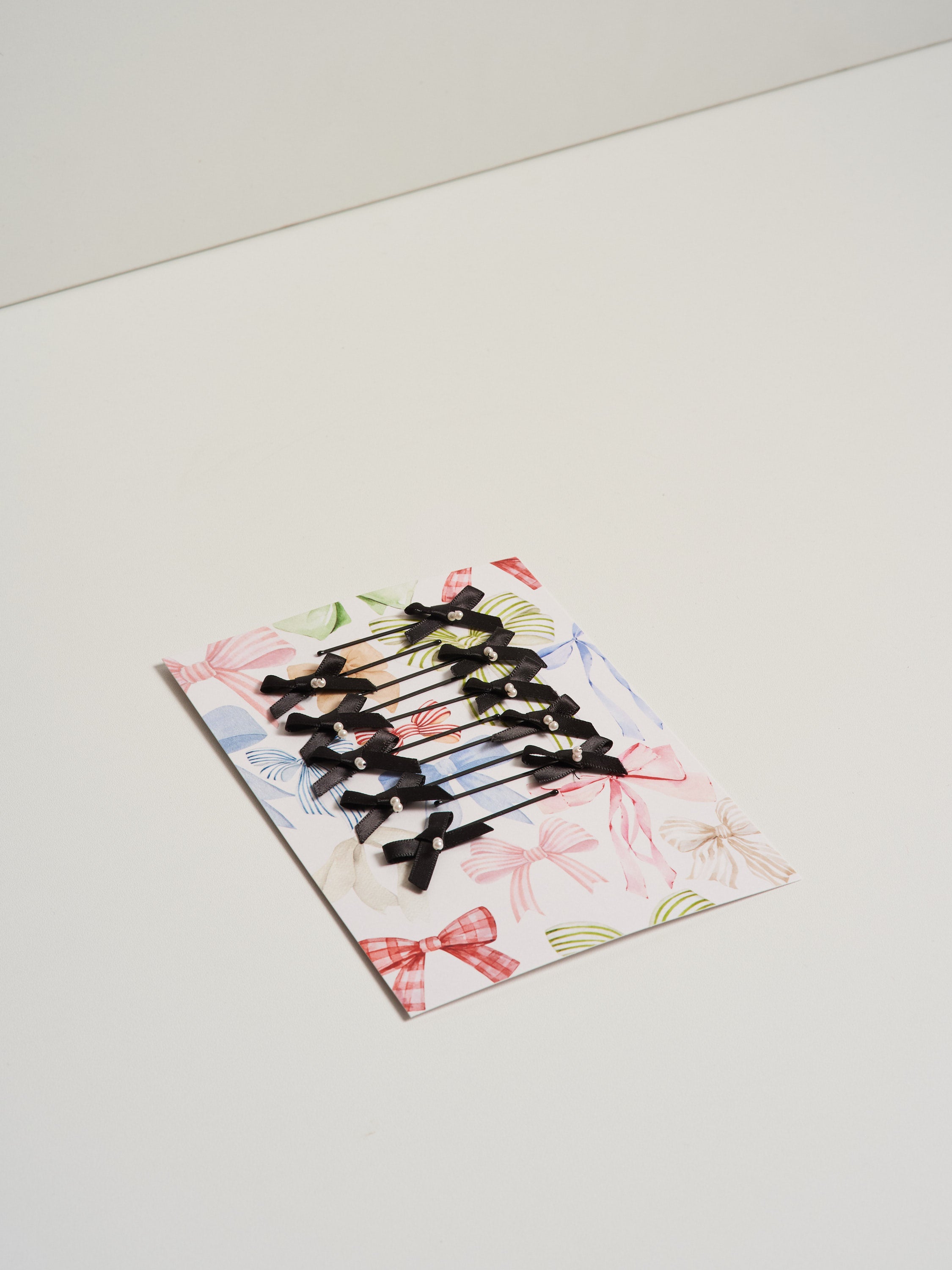 Black satin bow hair slides displayed on card stock and pictured on a white background.