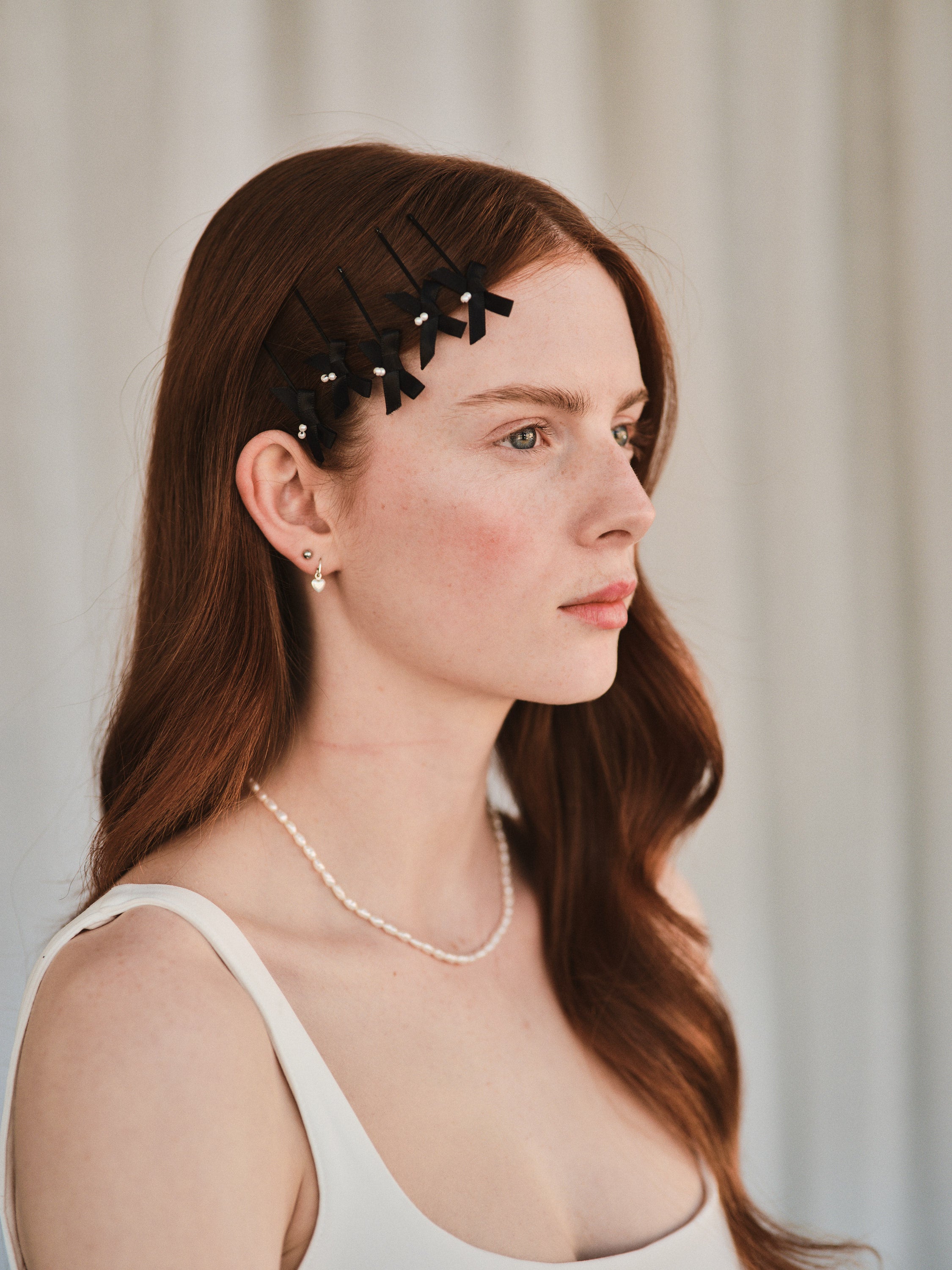 Model with long red hair wears black satin bow with pearl hair slides styled with a white evening dress.