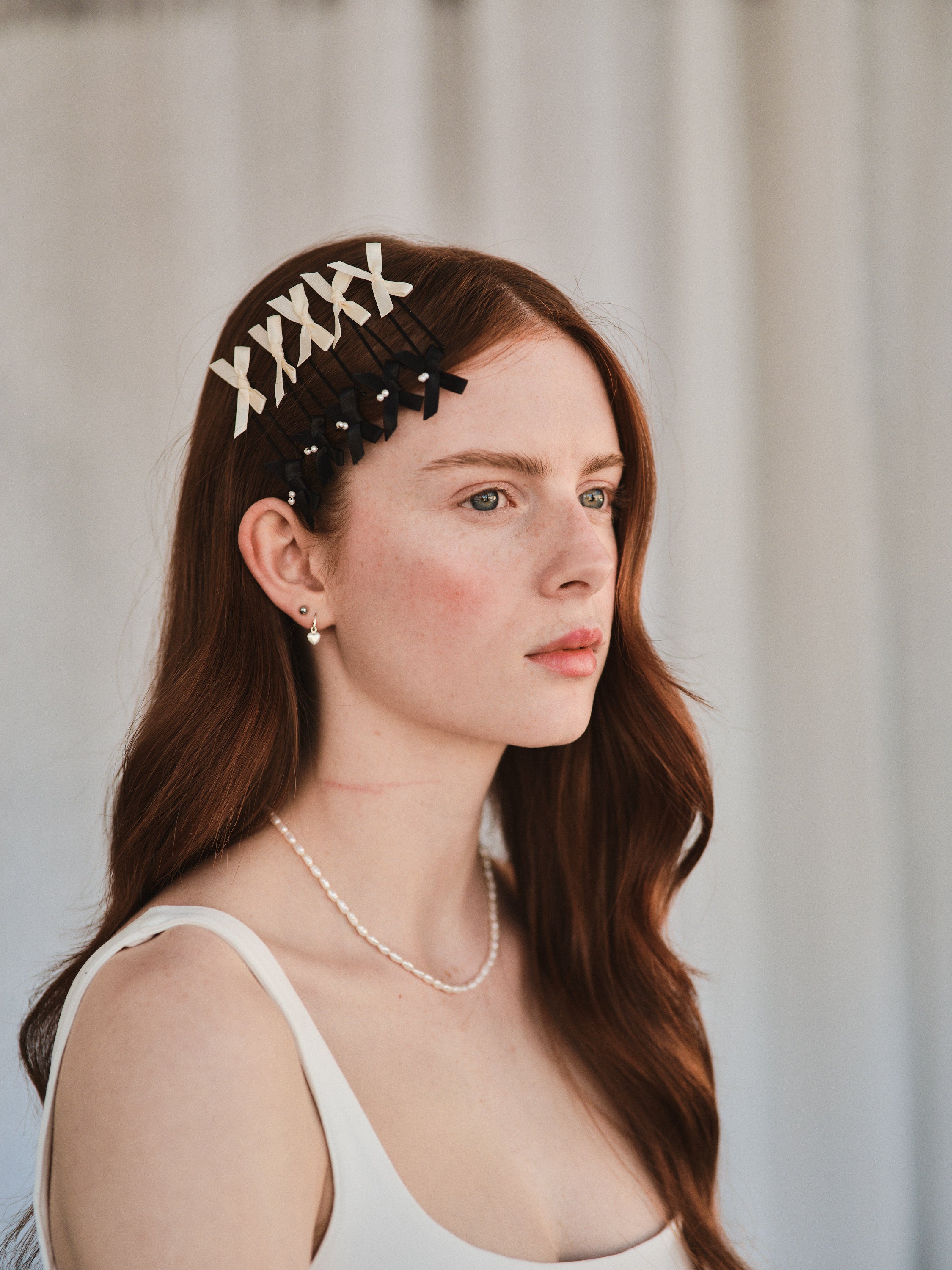Model with long red hair wears black satin bow with pearl hair slides styled with a white evening dress.