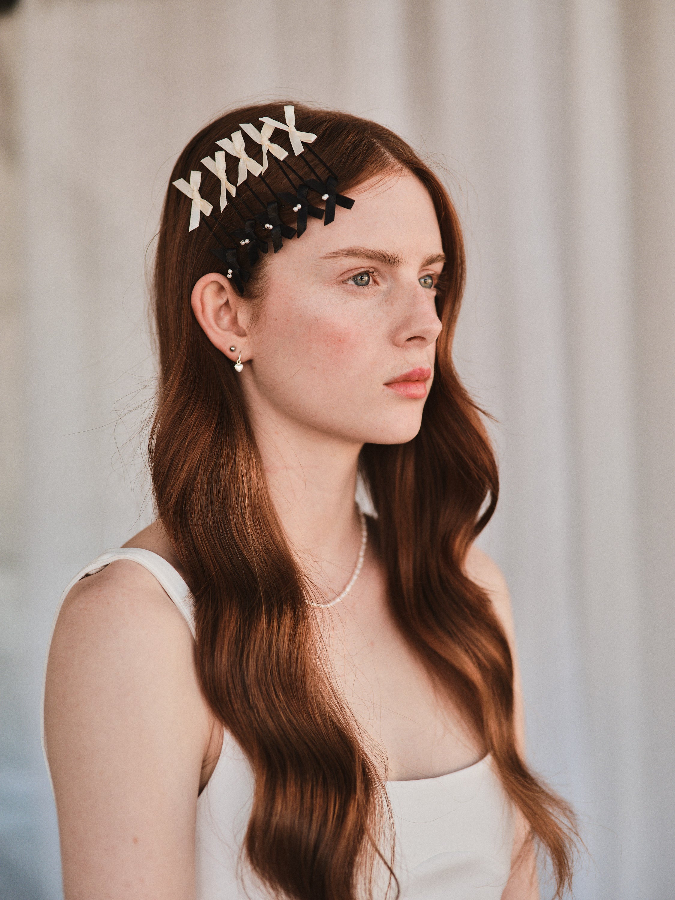 Model with long red hair wears black satin bow with pearl and white satin bow hair slides styled with a white evening dress.