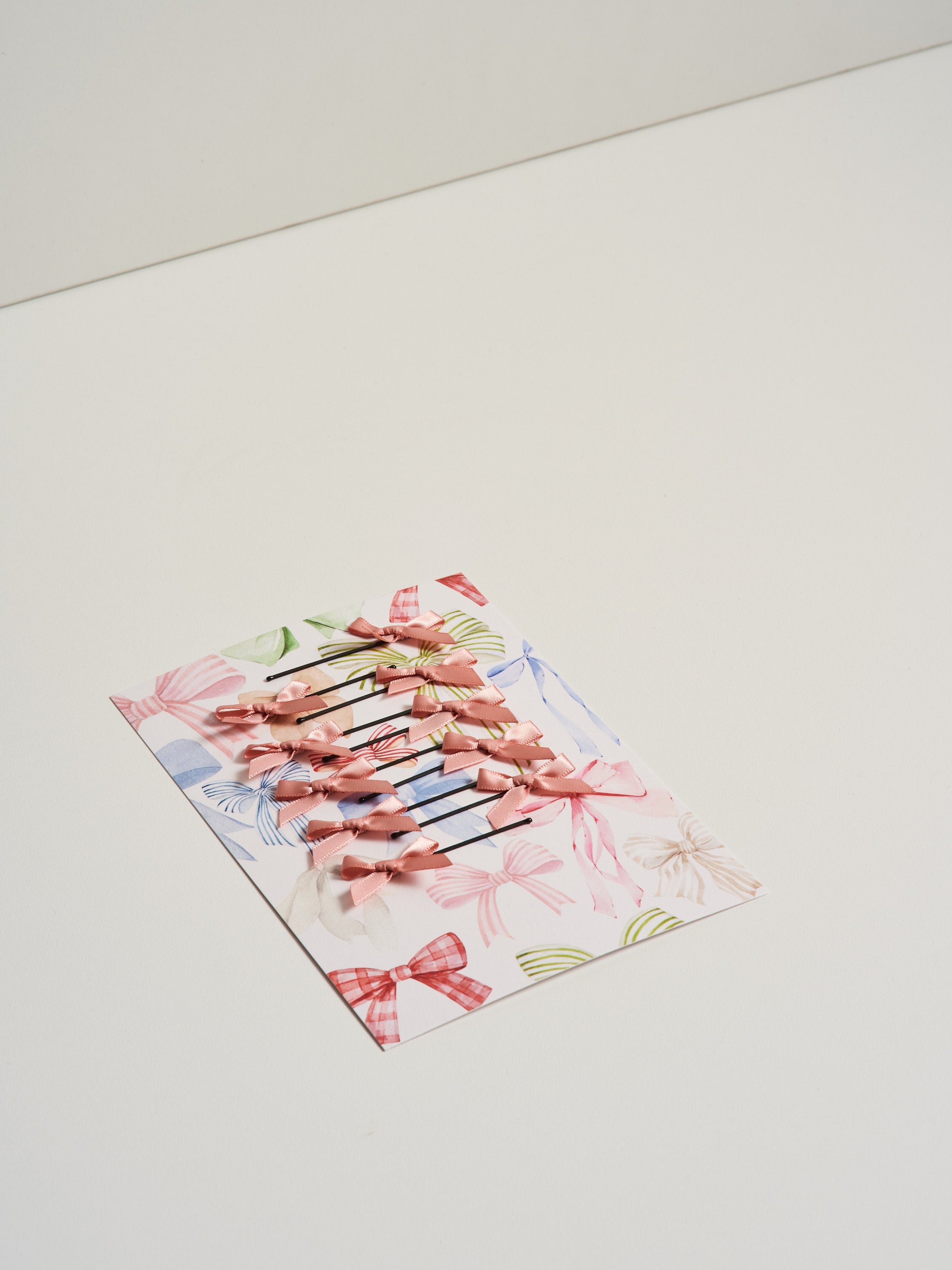 Light pink satin bow hair slides displayed on card stock and pictured on a white background.