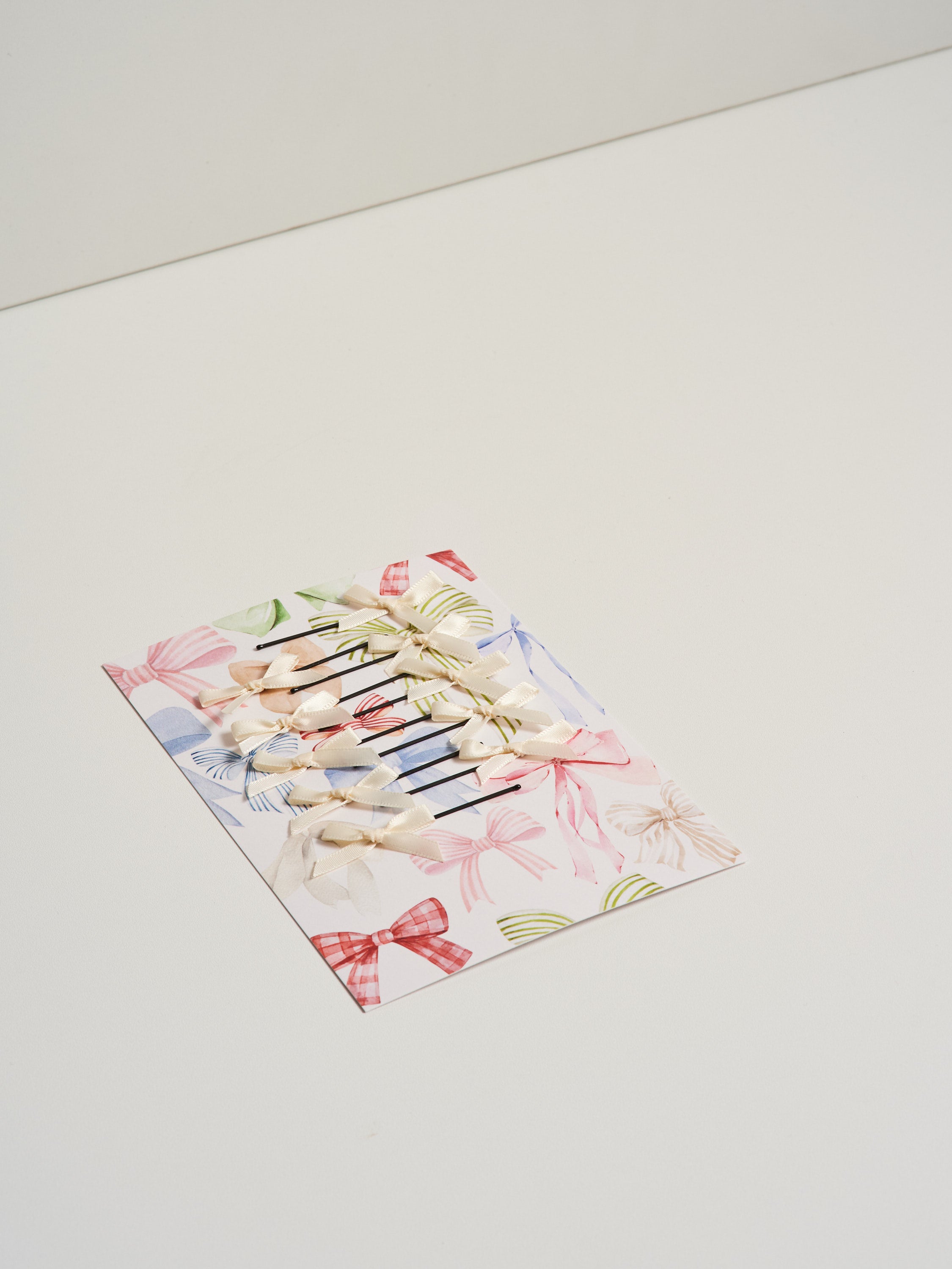 Off white satin bow hair slides displayed on card stock and pictured on a white background.
