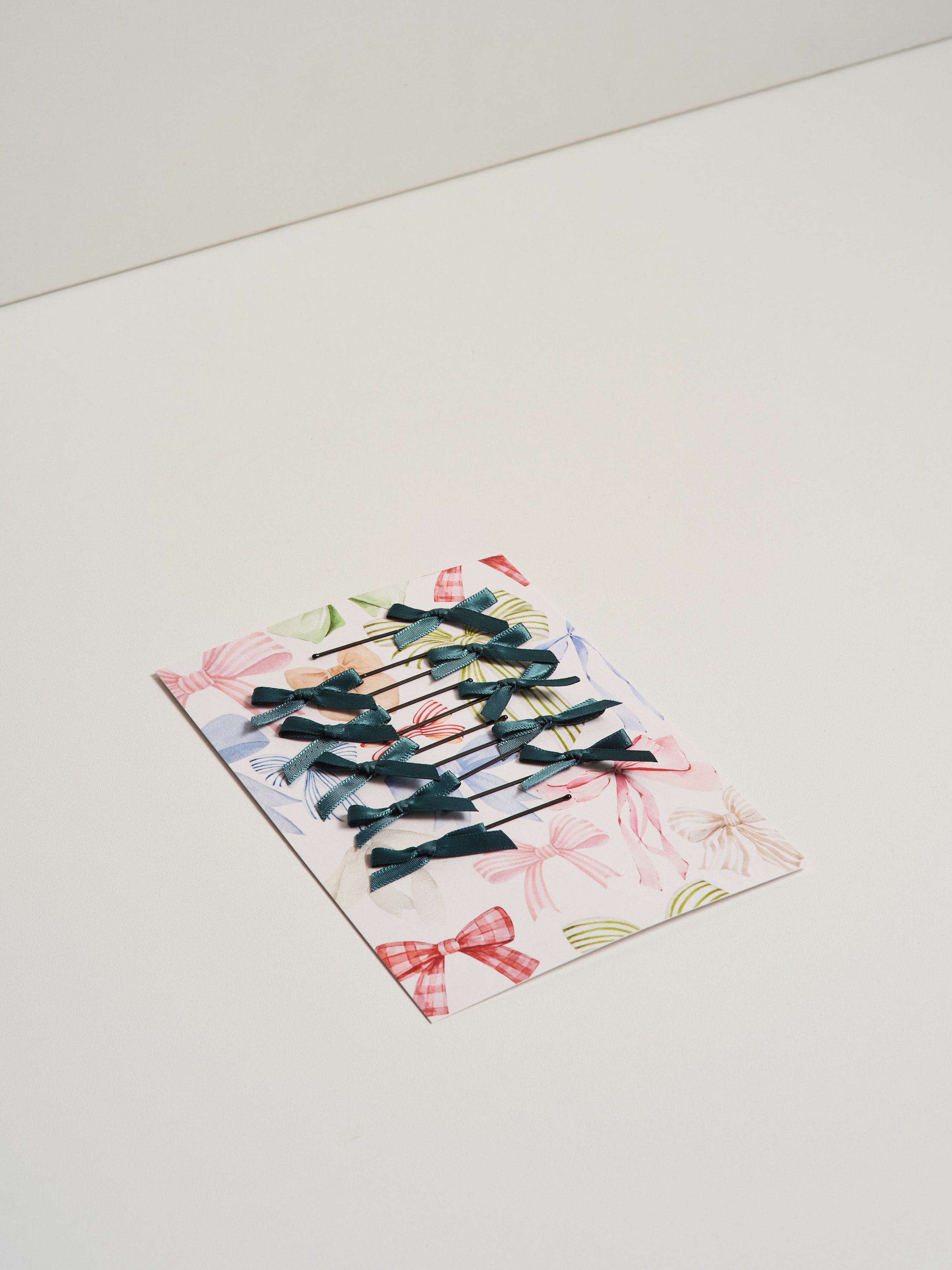 Dark green satin bow hair slides displayed on card stock and pictured on a white background.