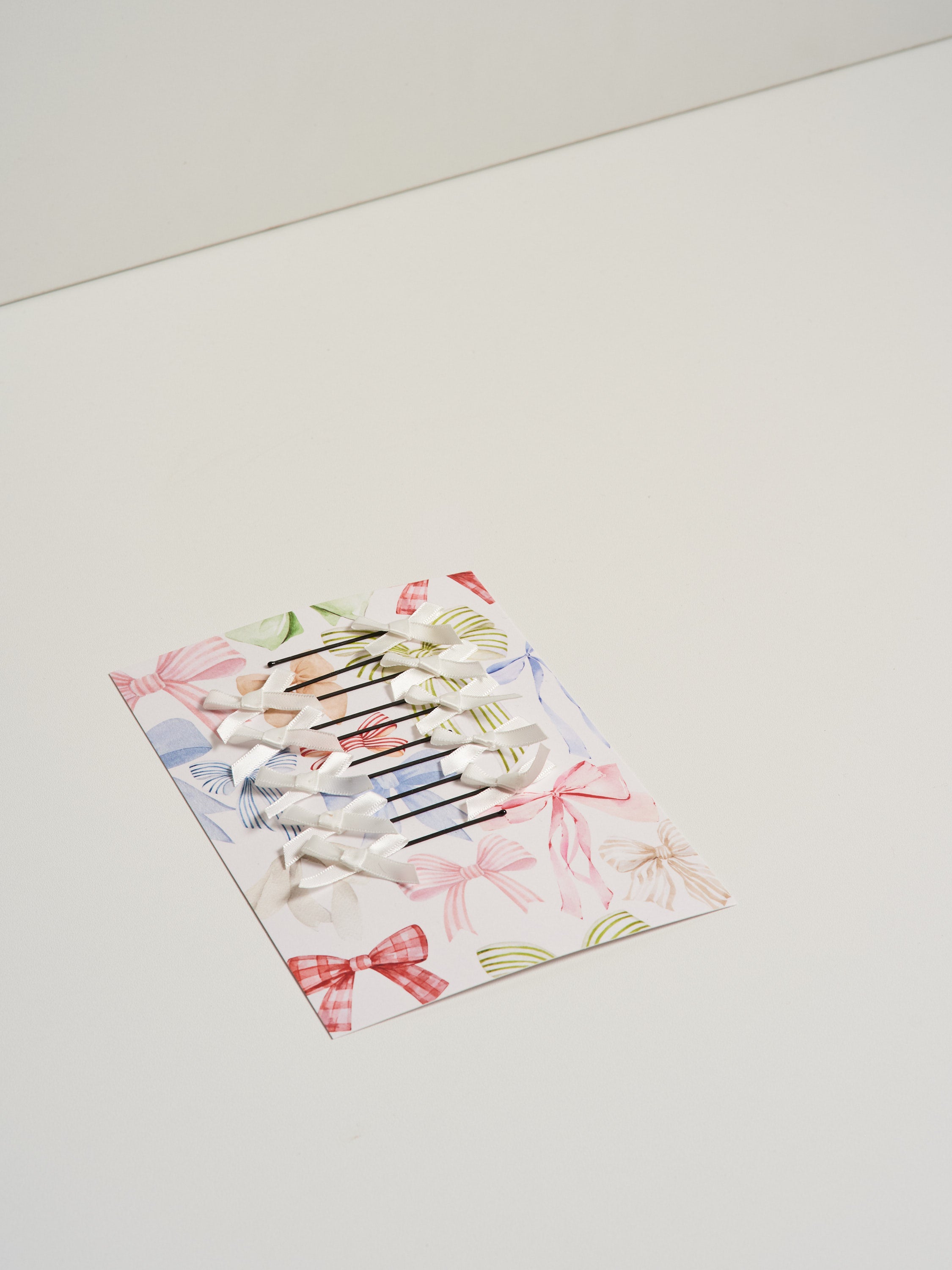 White satin bow hair slides displayed on card stock and pictured on a white background.