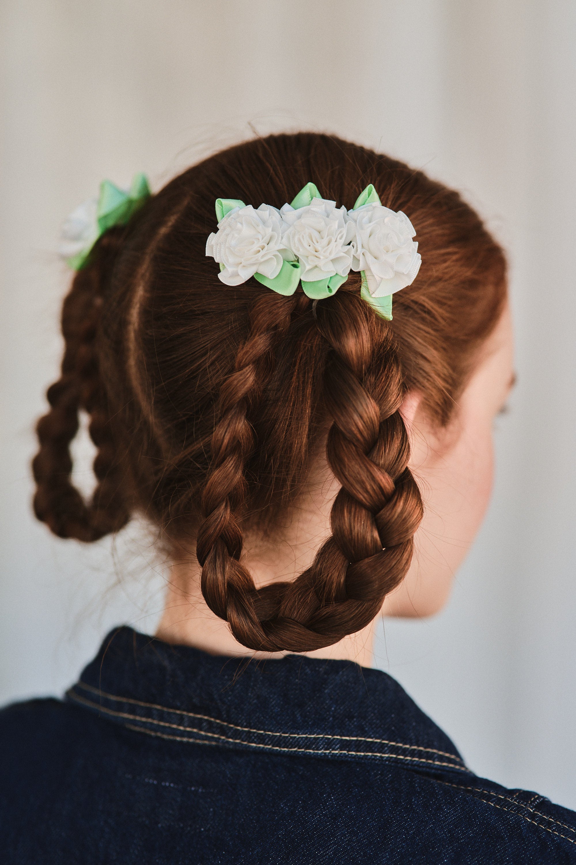 Model with braided pigtails wears white carnation flower cluster hair clips, styled with a denim jacket.