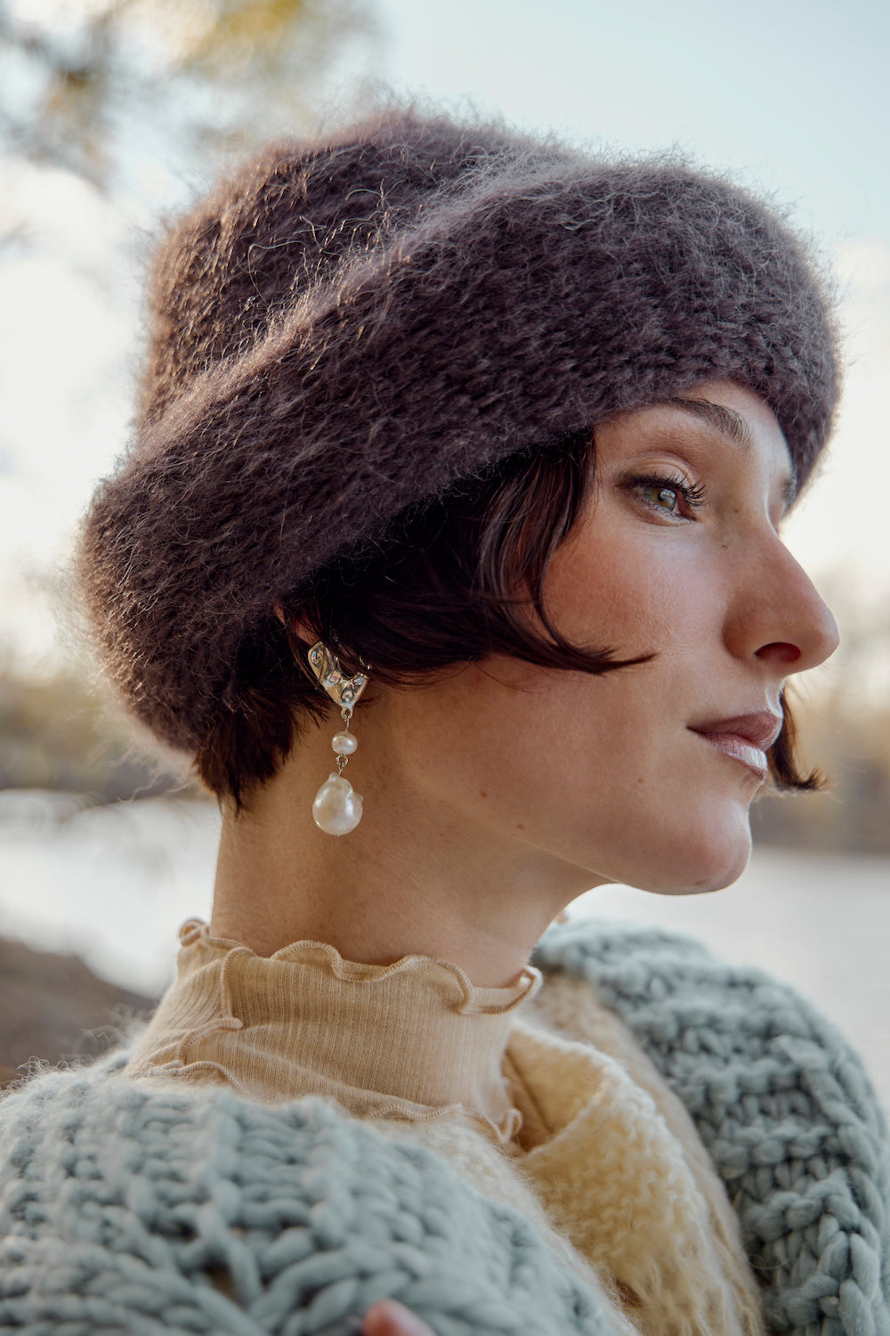 Model wearing dangling pearl earrings and a chunky knit sweater, paired with a chocolate brown mohair beanie by Heirloom Hats, creating a stylish, cozy look.