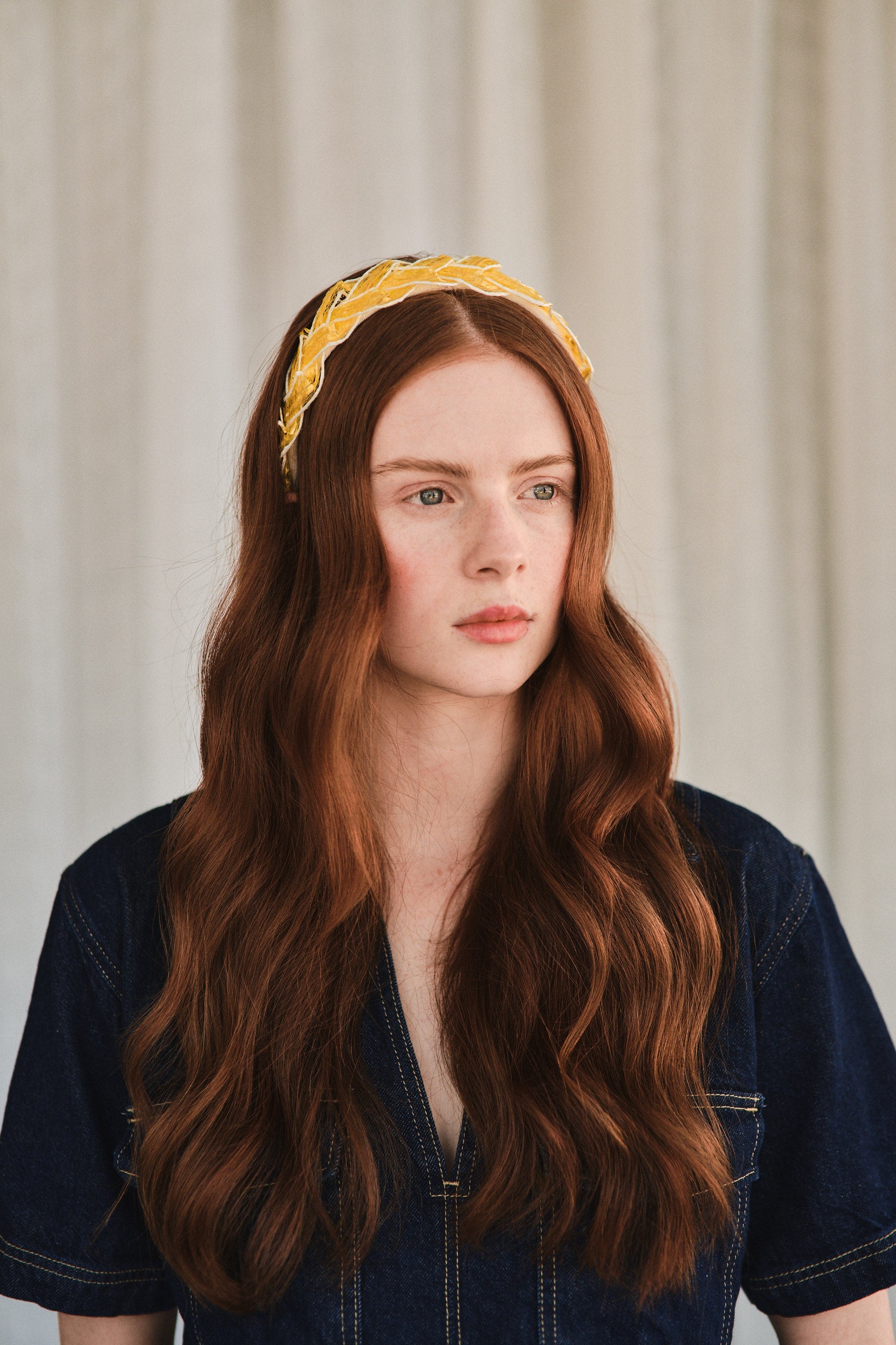 Model with long red hair wears yellow straw headband, styled with a denim jacket.