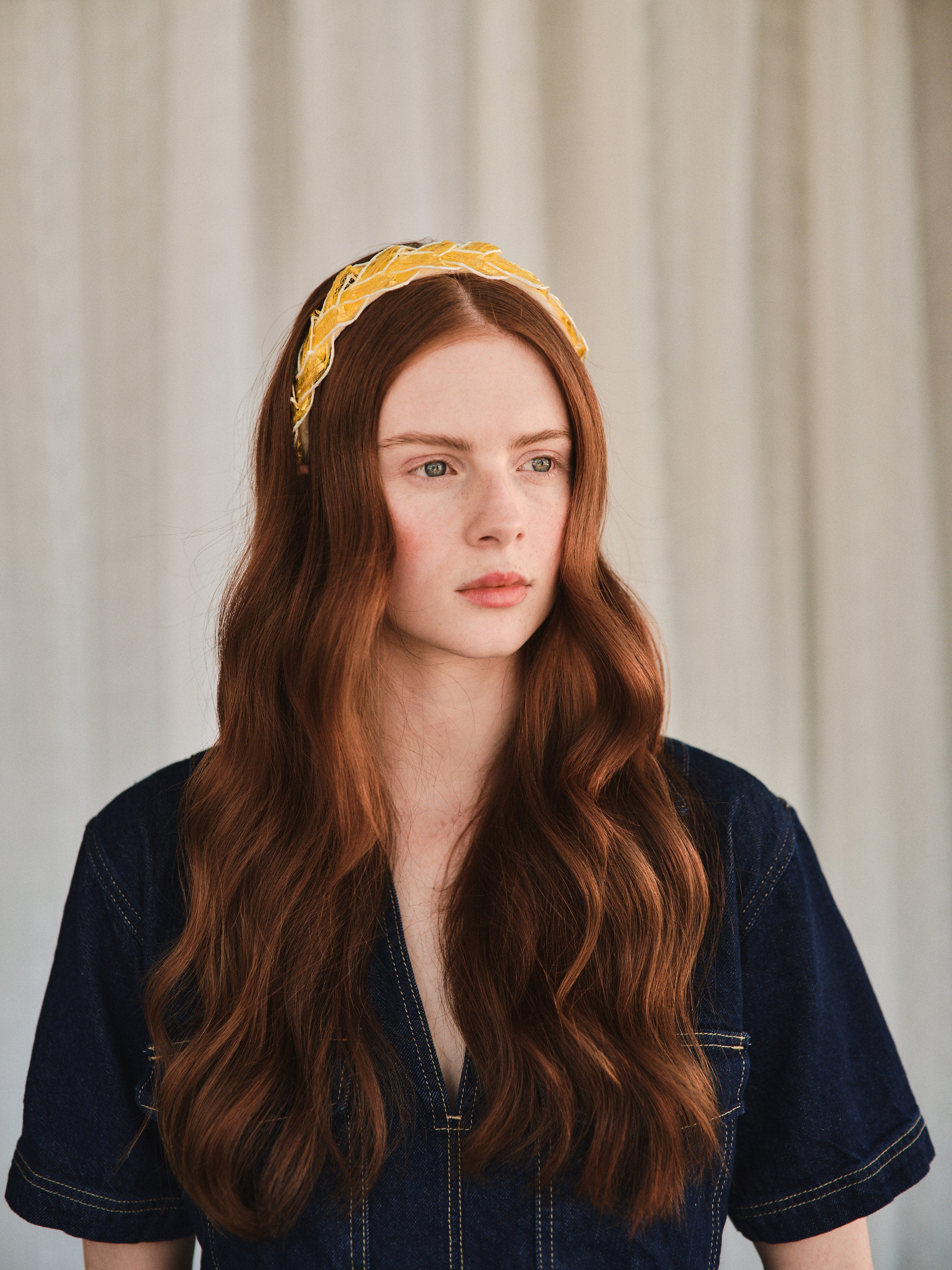 Model with long red hair wears yellow straw headband, styled with a denim jacket.