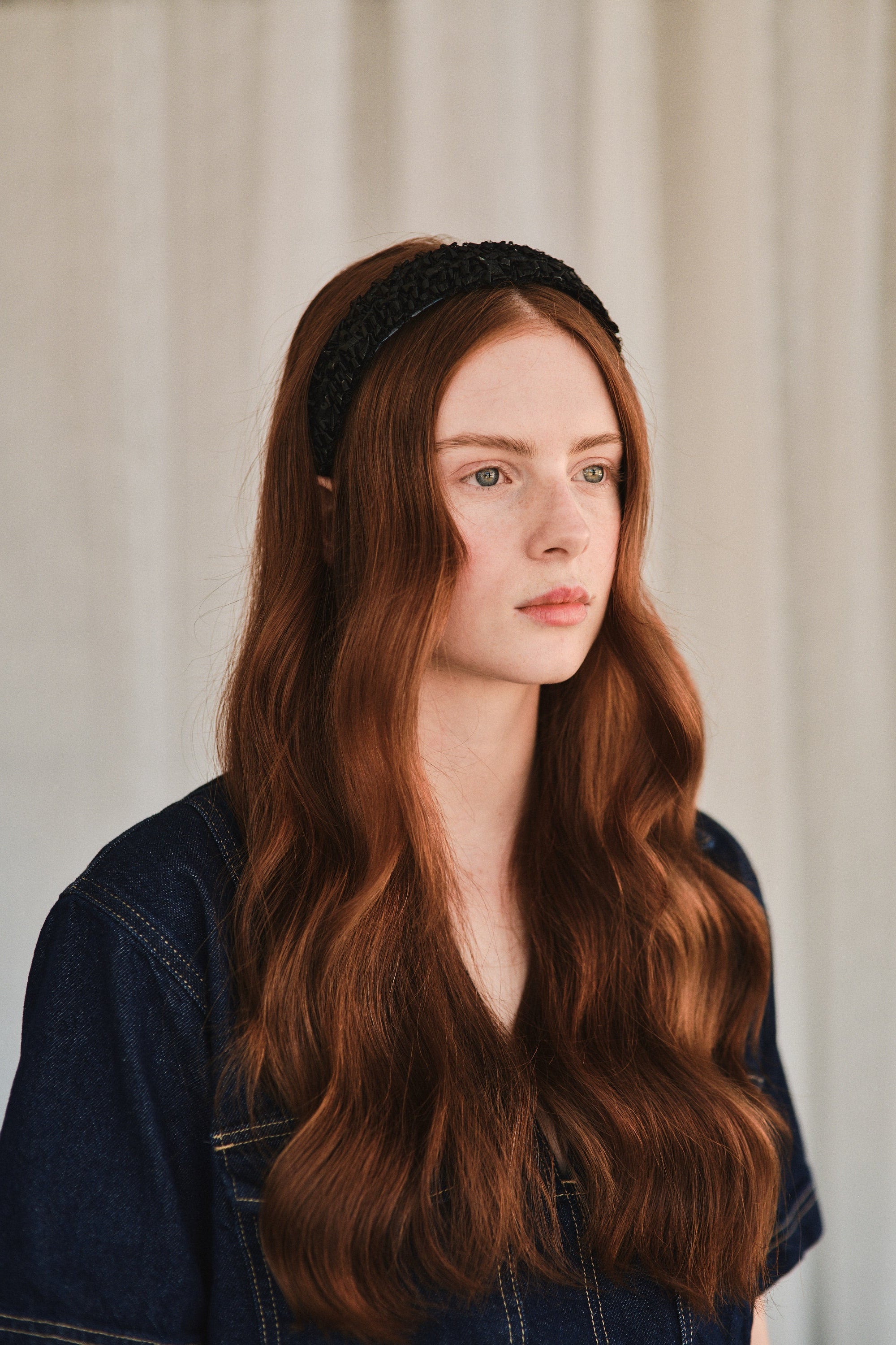 Model with long red hair wears black straw headband, styled with a denim jacket.