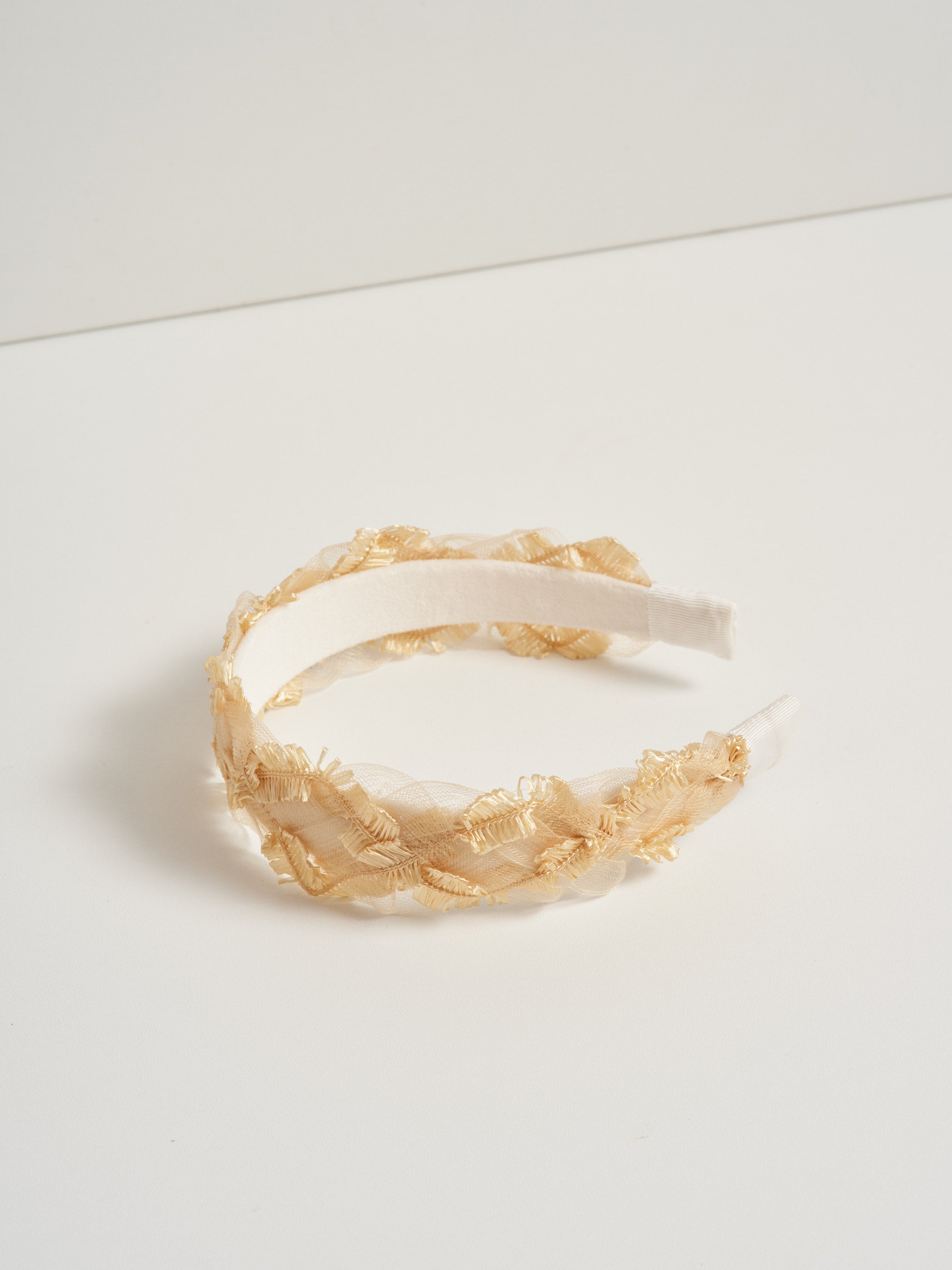 A gold coloured headband made with deadstock straw, pictured on a white background.