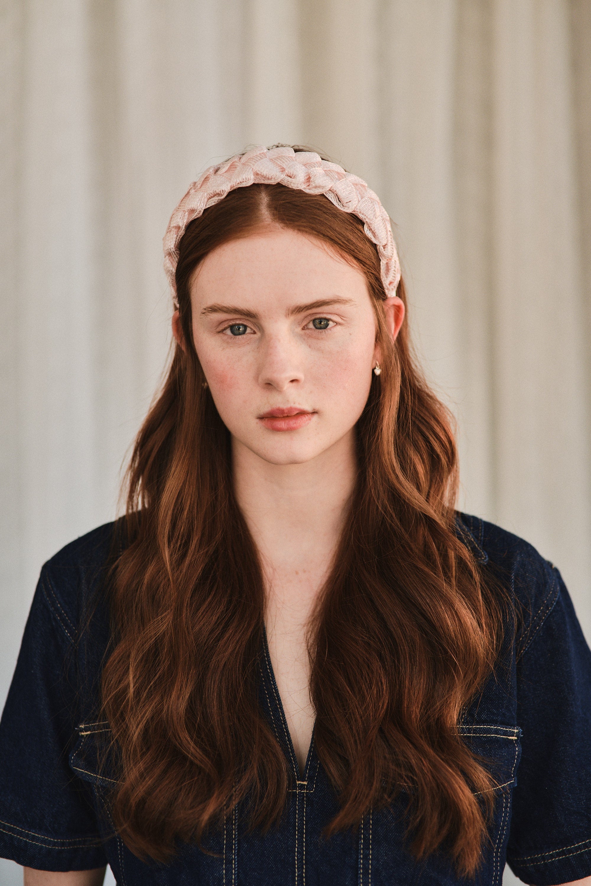 Model with long red hair wears a pink headband made with deadstock straw, styled with a denim jacket.