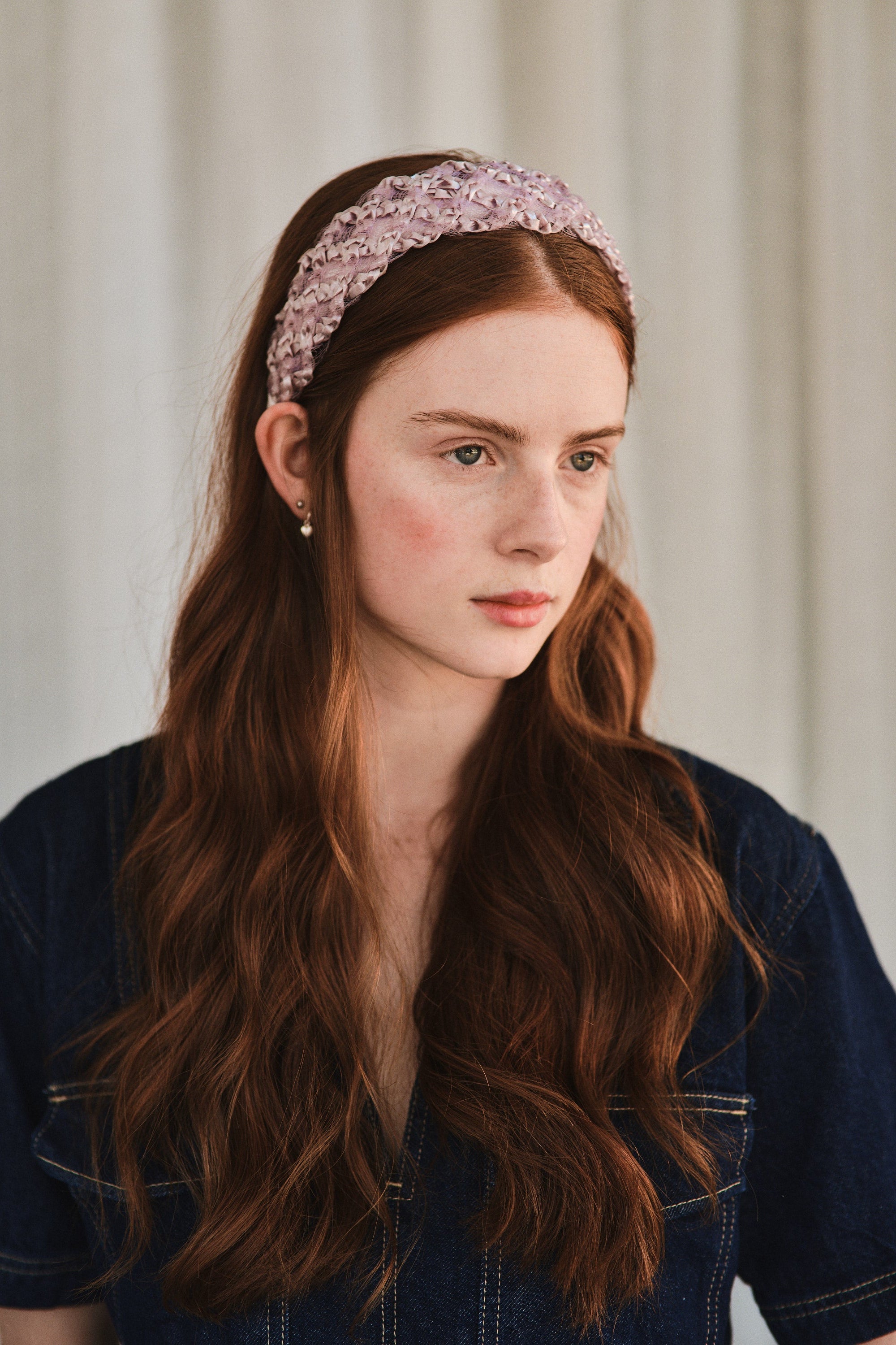 Model with long red hair wears a lilac headband made with deadstock straw, styled with a denim jacket.