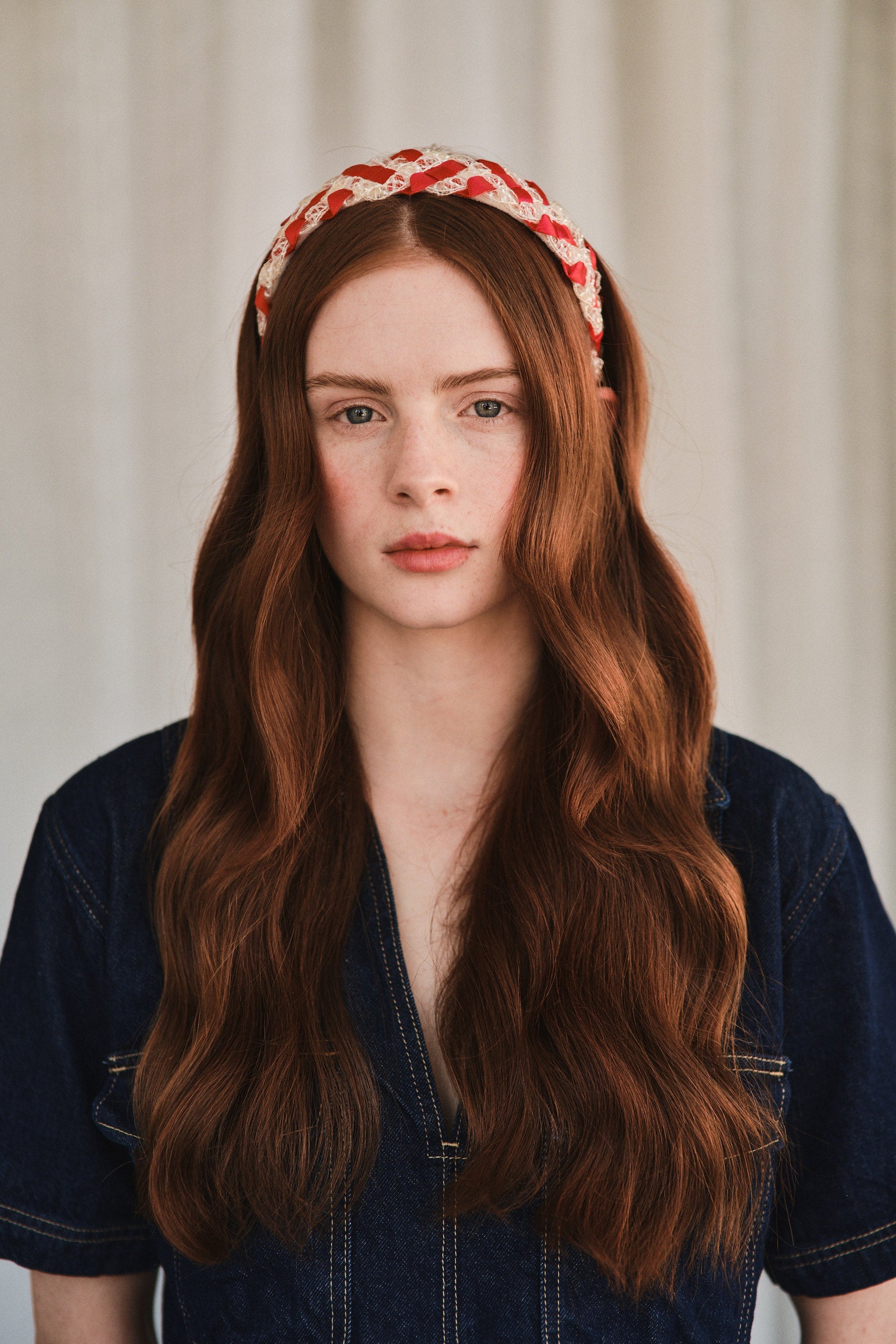 Model with long red hair wears red and white vintage straw headband, styled with a denim jacket.
