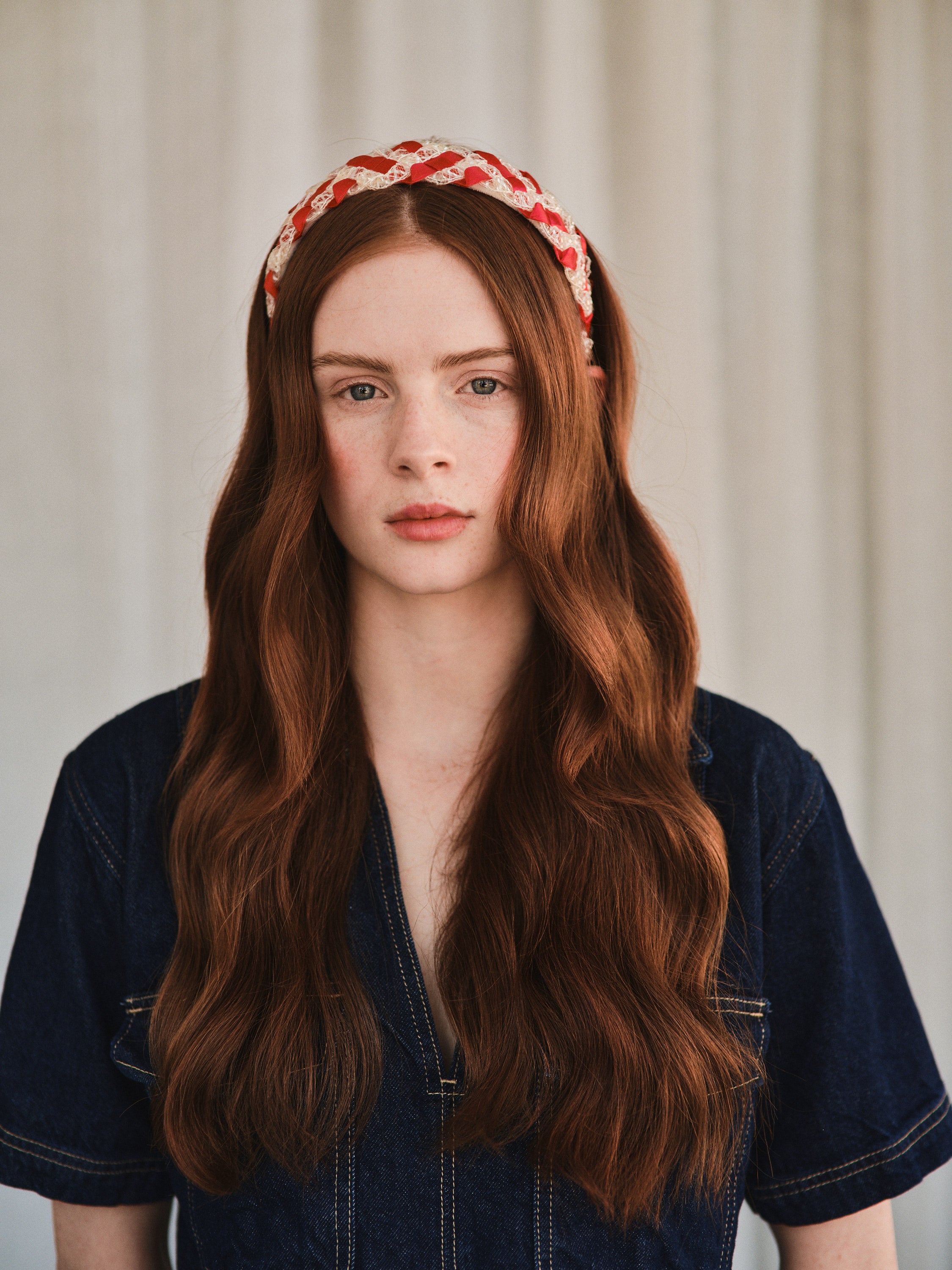 Model with long red hair wears red and white vintage straw headband, styled with a denim jacket.