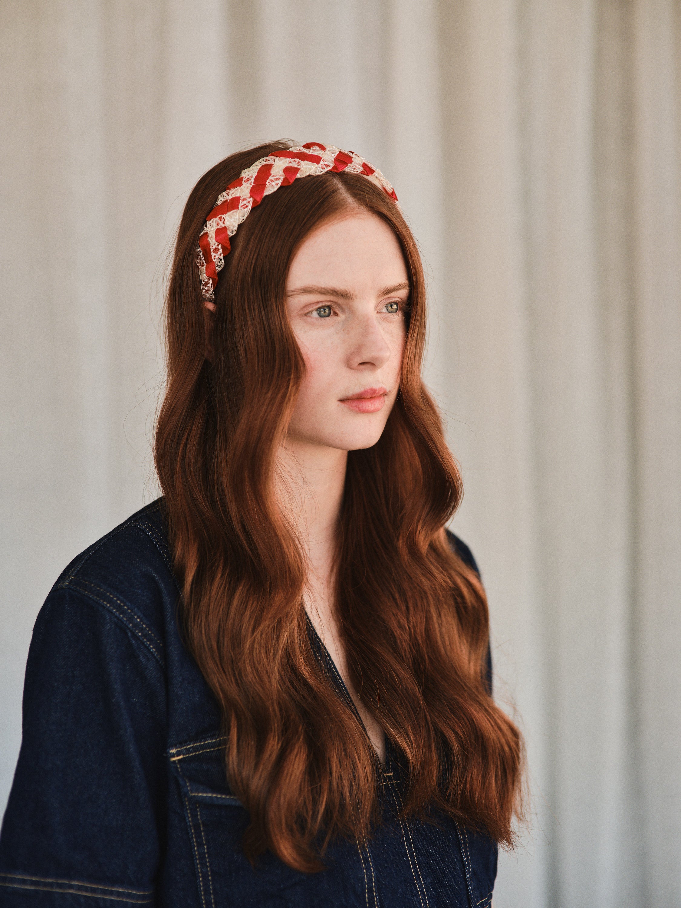 Model with long red hair wears red and white vintage straw headband, styled with a denim jacket.