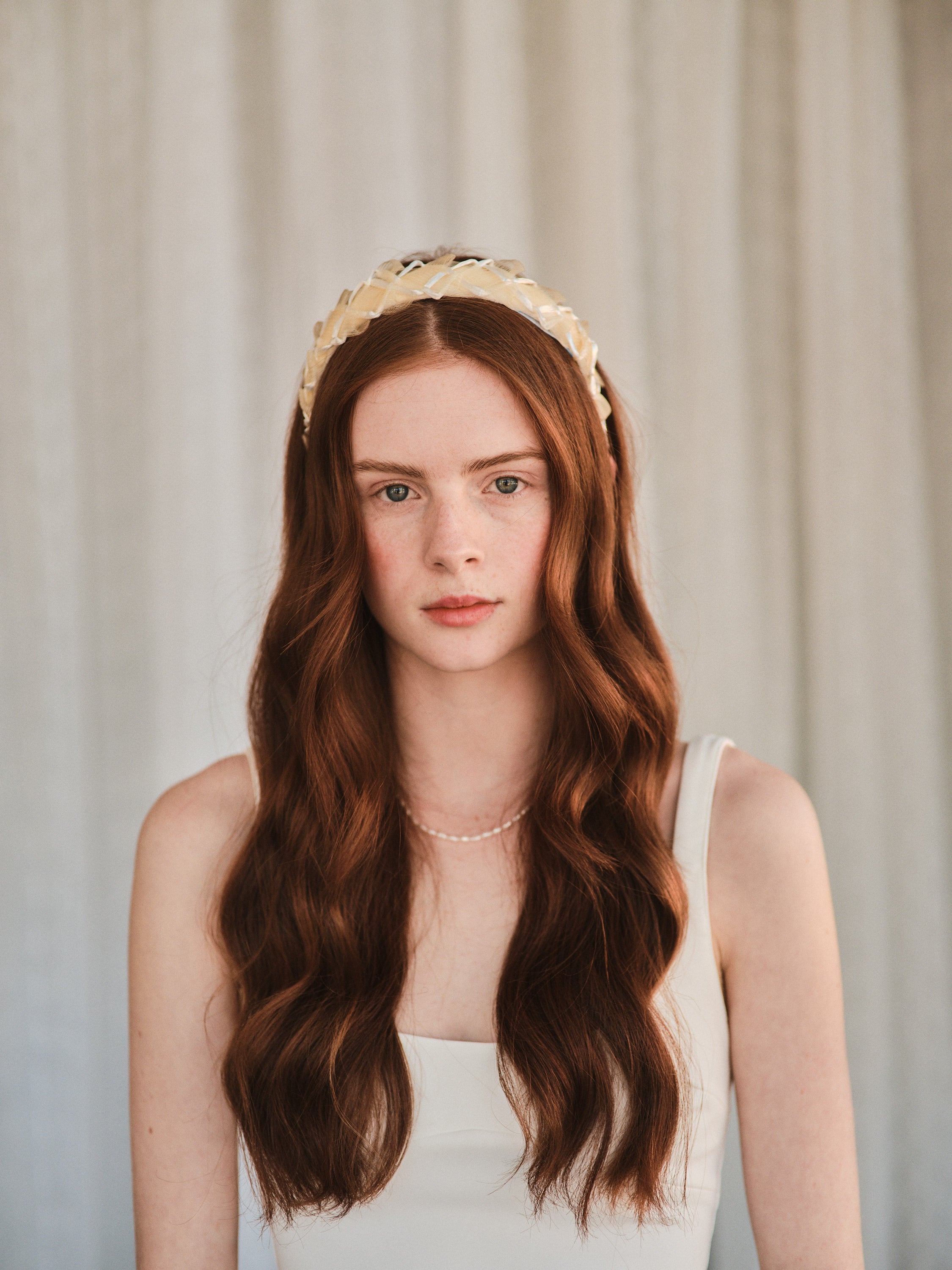 Model with long red hair wears an off white headband made with deadstock straw, styled with a white tank dress.