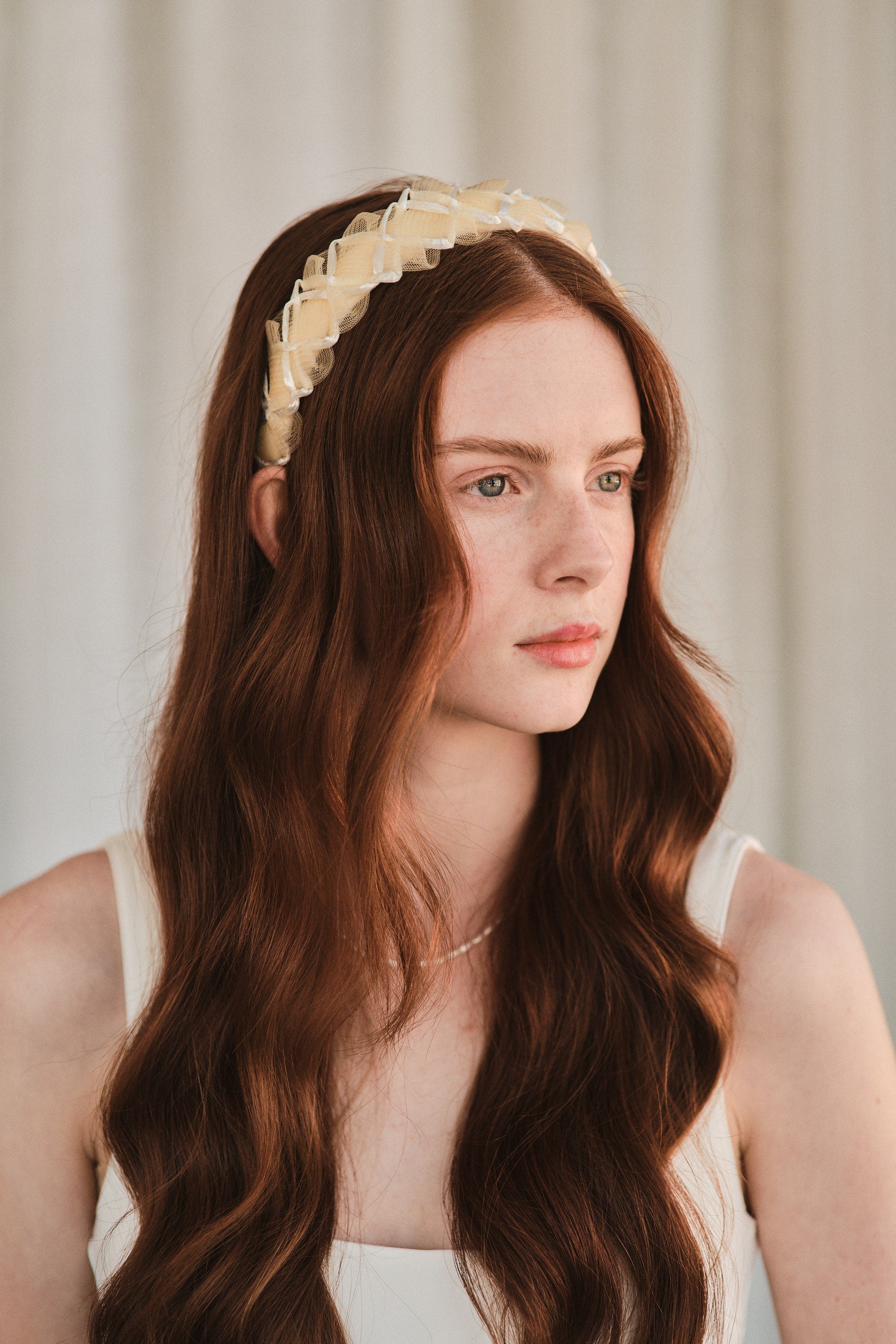 Model with long red hair wears an off white headband made with deadstock straw, styled with a white tank dress.