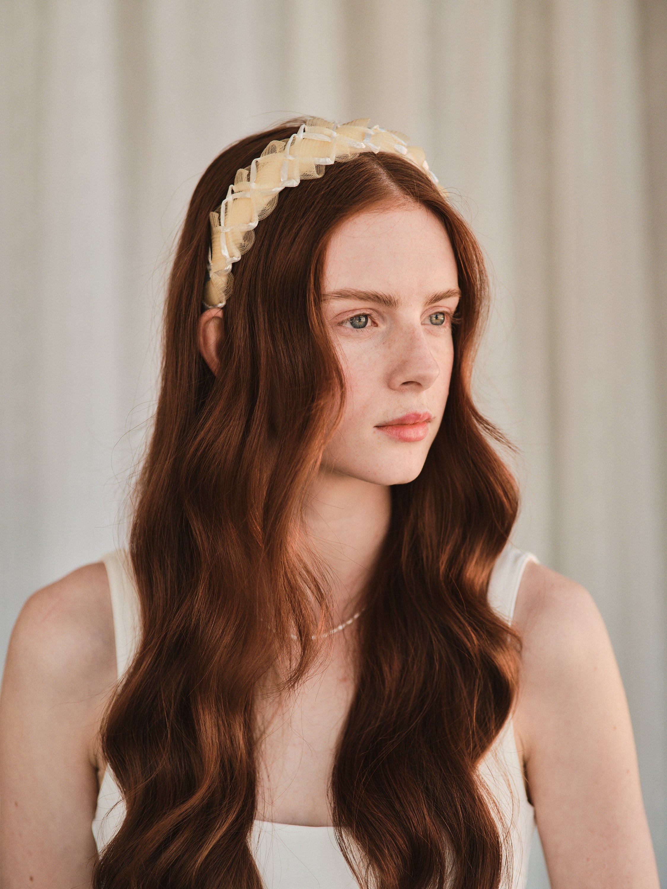 Model with long red hair wears an off white headband made with deadstock straw, styled with a white tank dress.