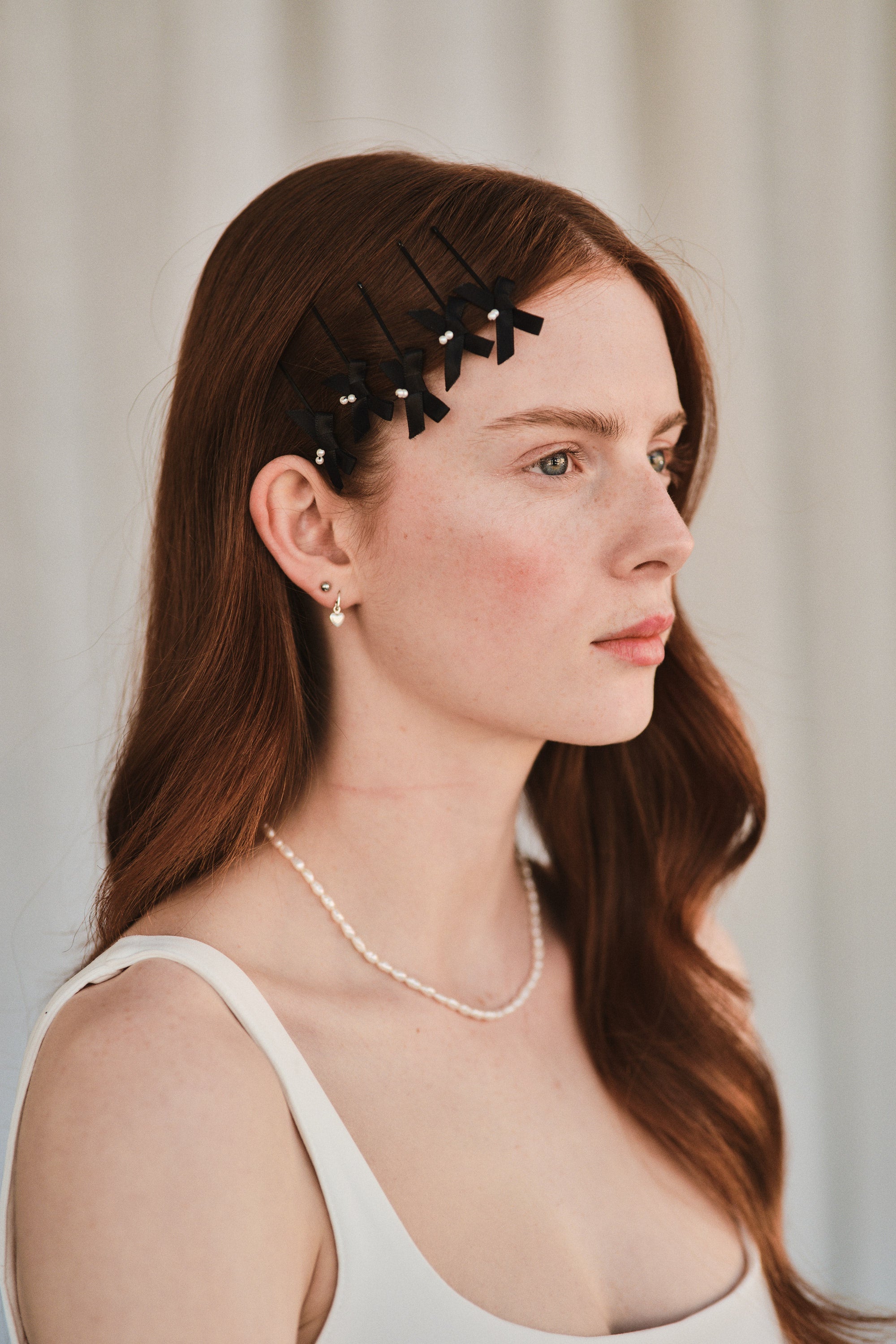 Model with long red hair wears black satin bow with pearl hair slides styled with a white evening dress.