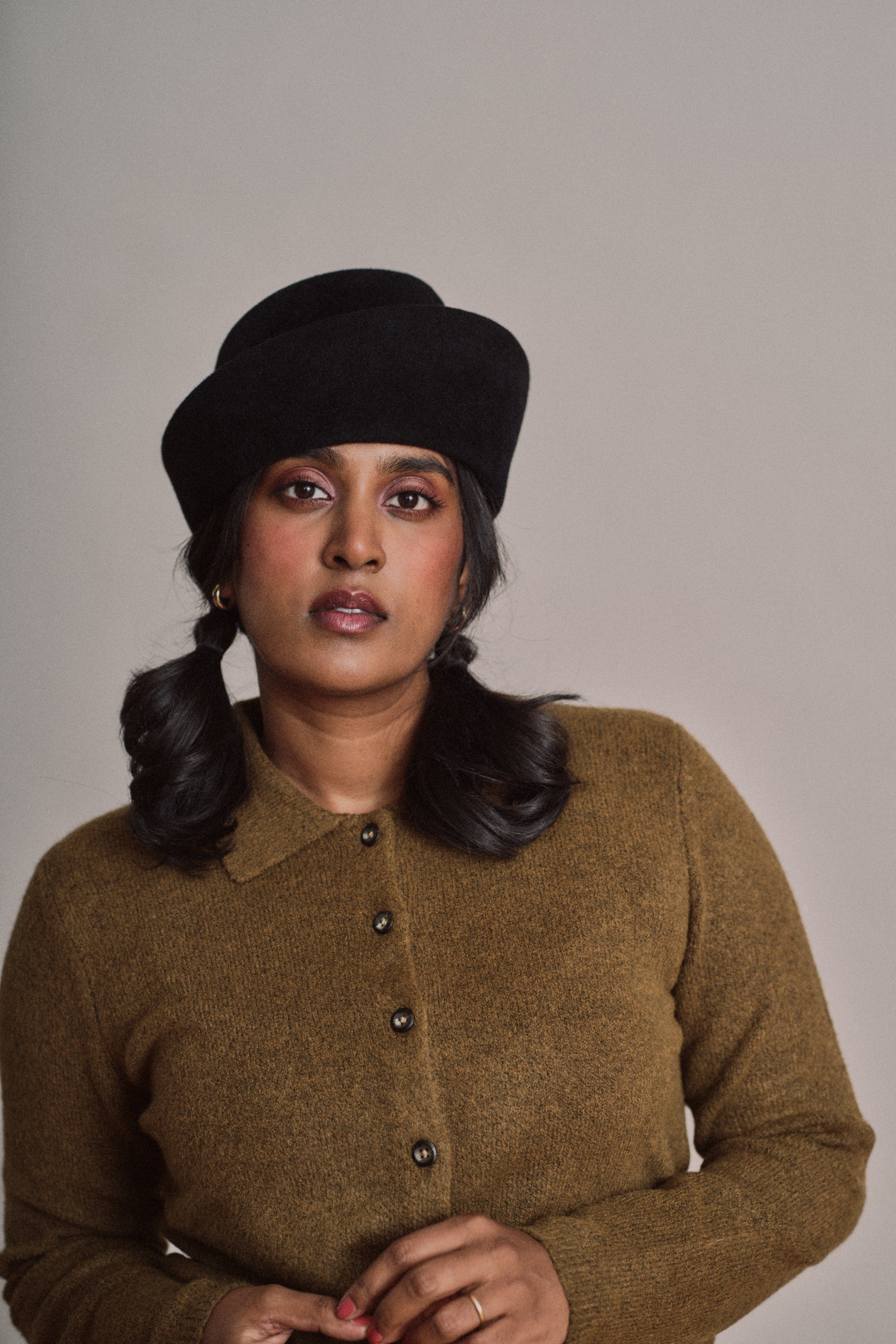 Woman wearing a black hat and brown sweater against a plain background