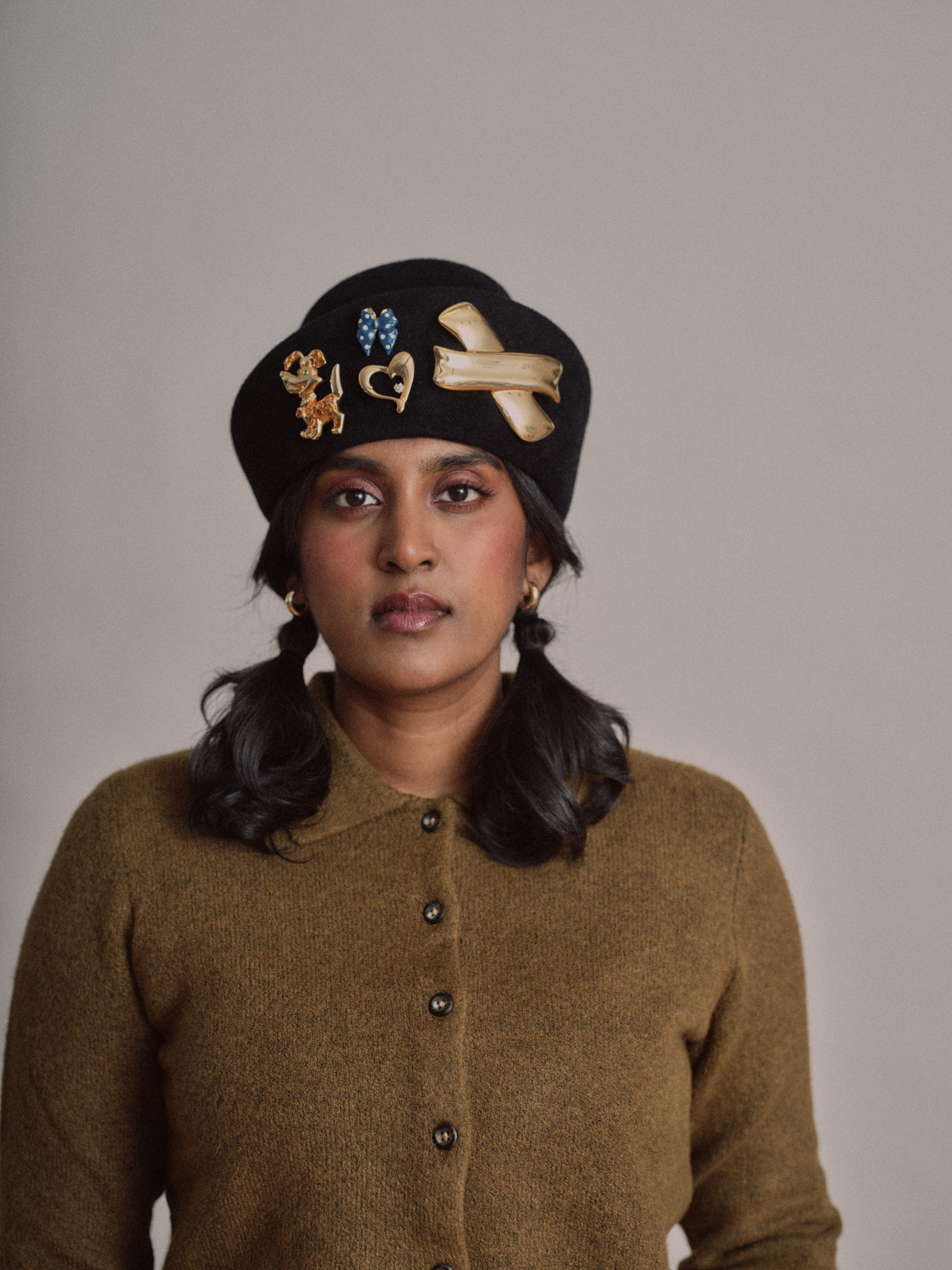 Person wearing a black beret with decorative brooches against a plain background