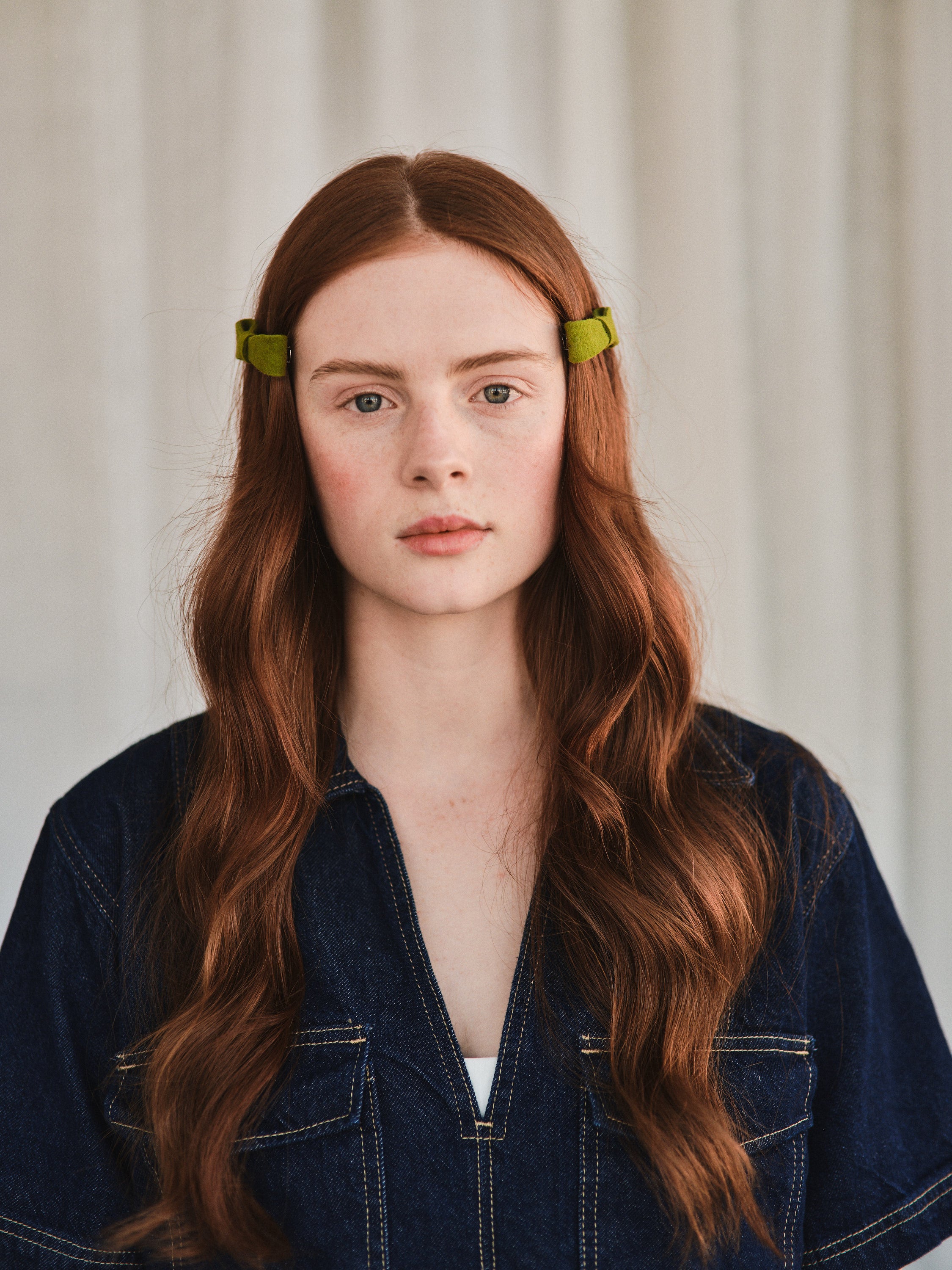 Model with long natural red hair wears green felt bow hair clip on each side of her head, styled with denim jacket.