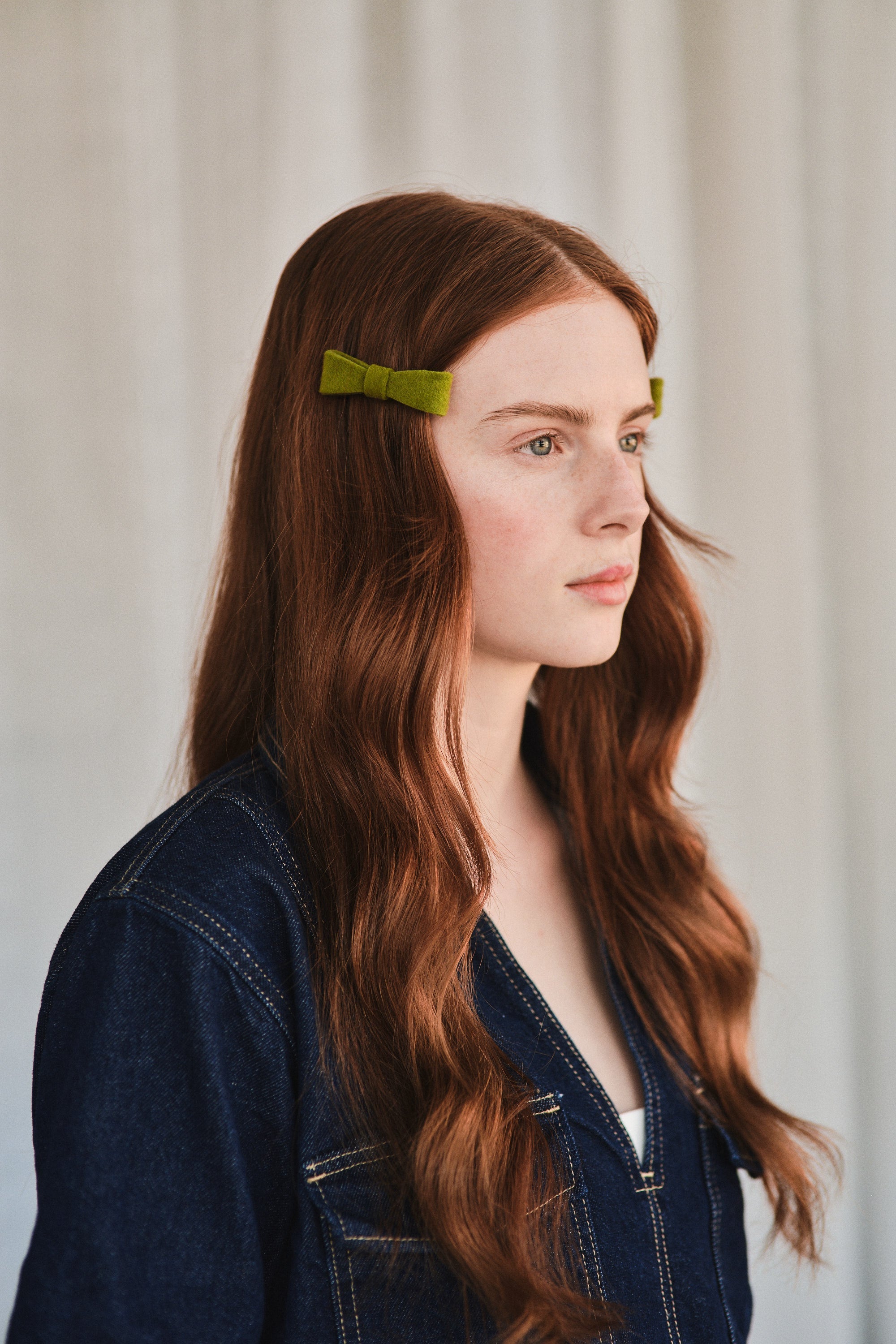 Model with long natural red hair wears green felt bow hair clip, styled with denim jacket.