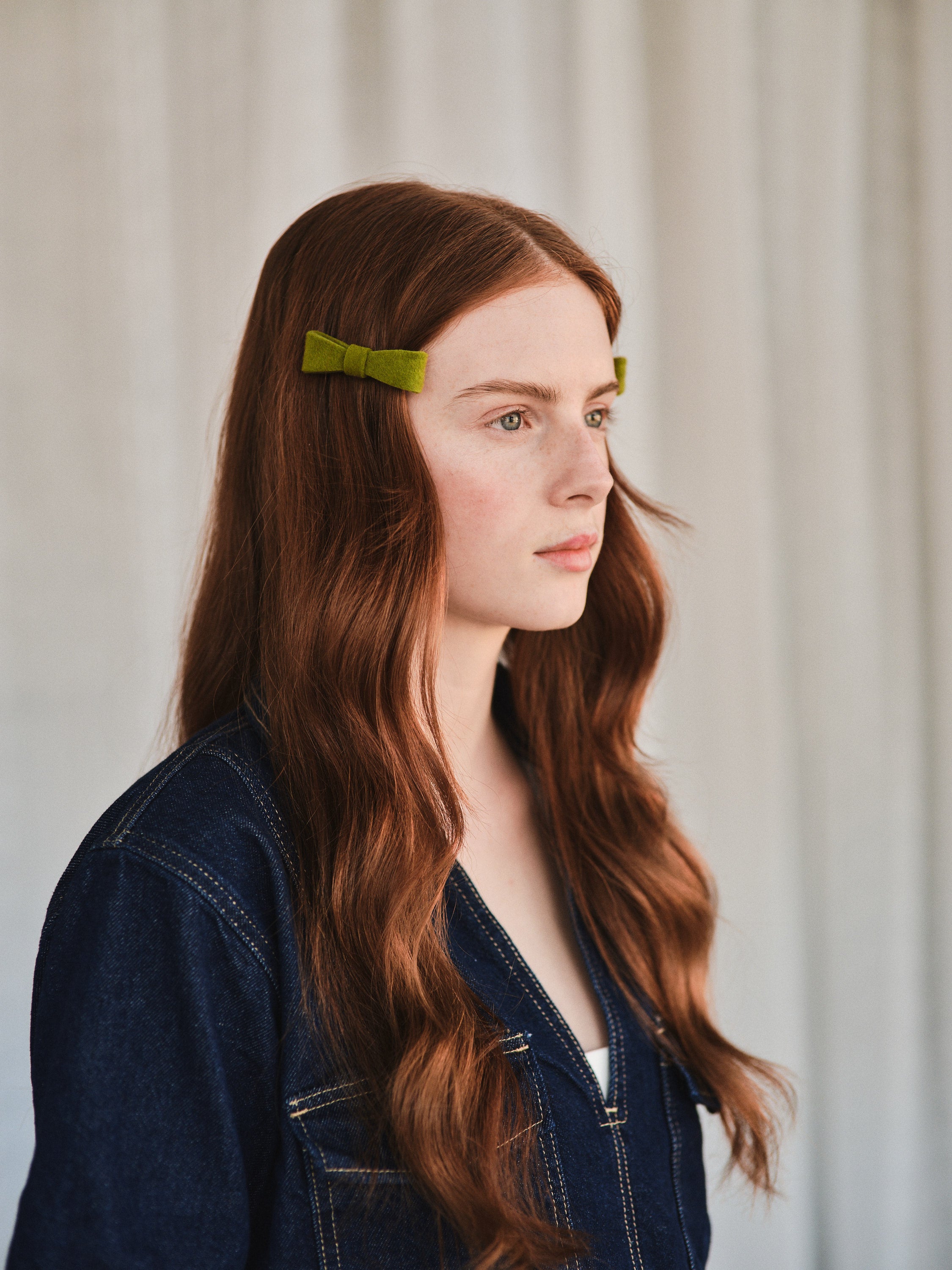 Model with long natural red hair wears green felt bow hair clip, styled with denim jacket.