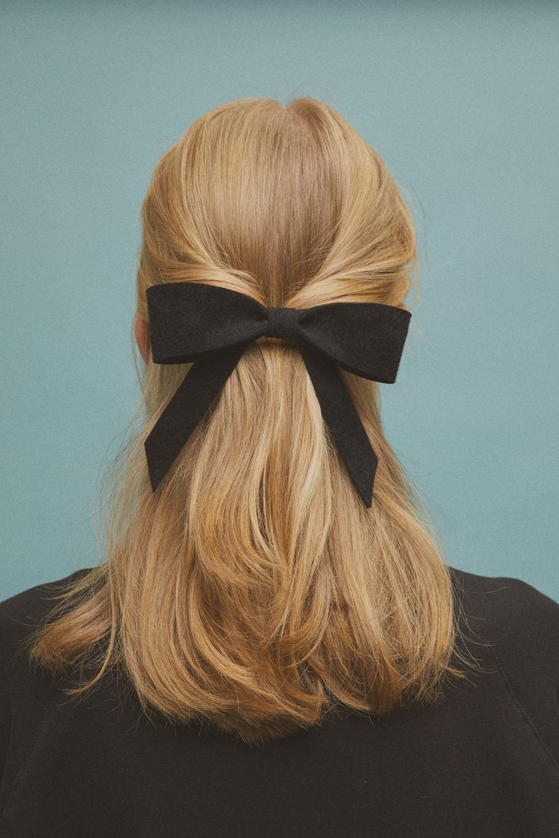 Black felt hair bow attached to a large French barrette, styled on mid length blond hair. Handmade, sustainable accessory by Heirloom Hats.