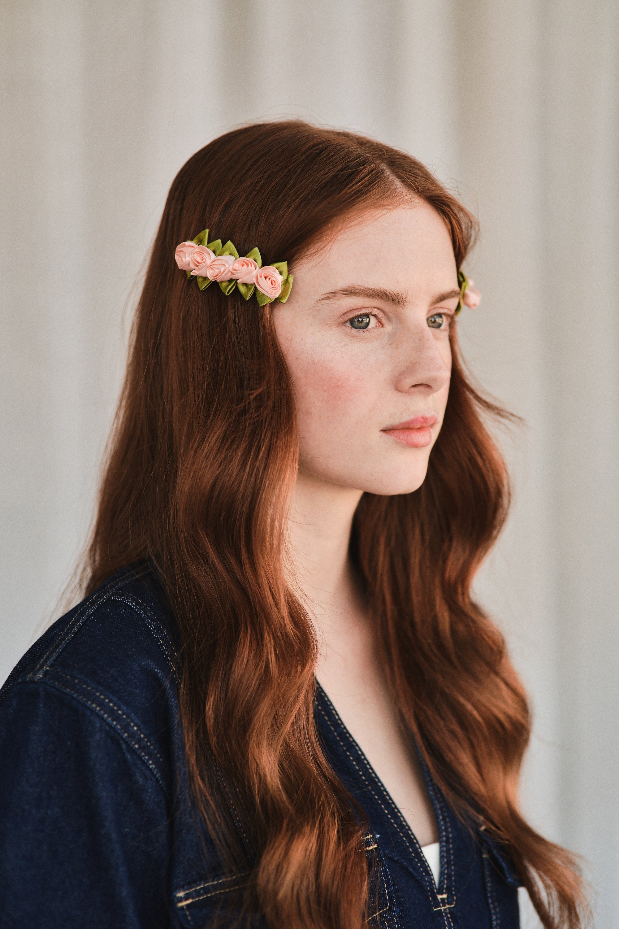 Model with long red hair wears light pink satin rosette hair clips, styled with a denim jacket.