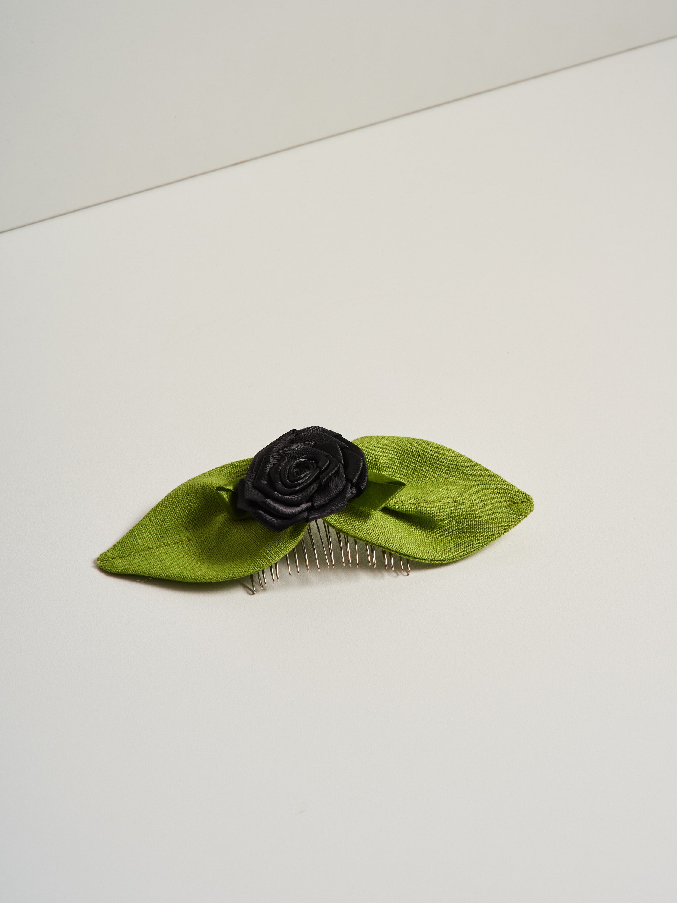Black satin rosette and green linen leaves, pictured on a white background.