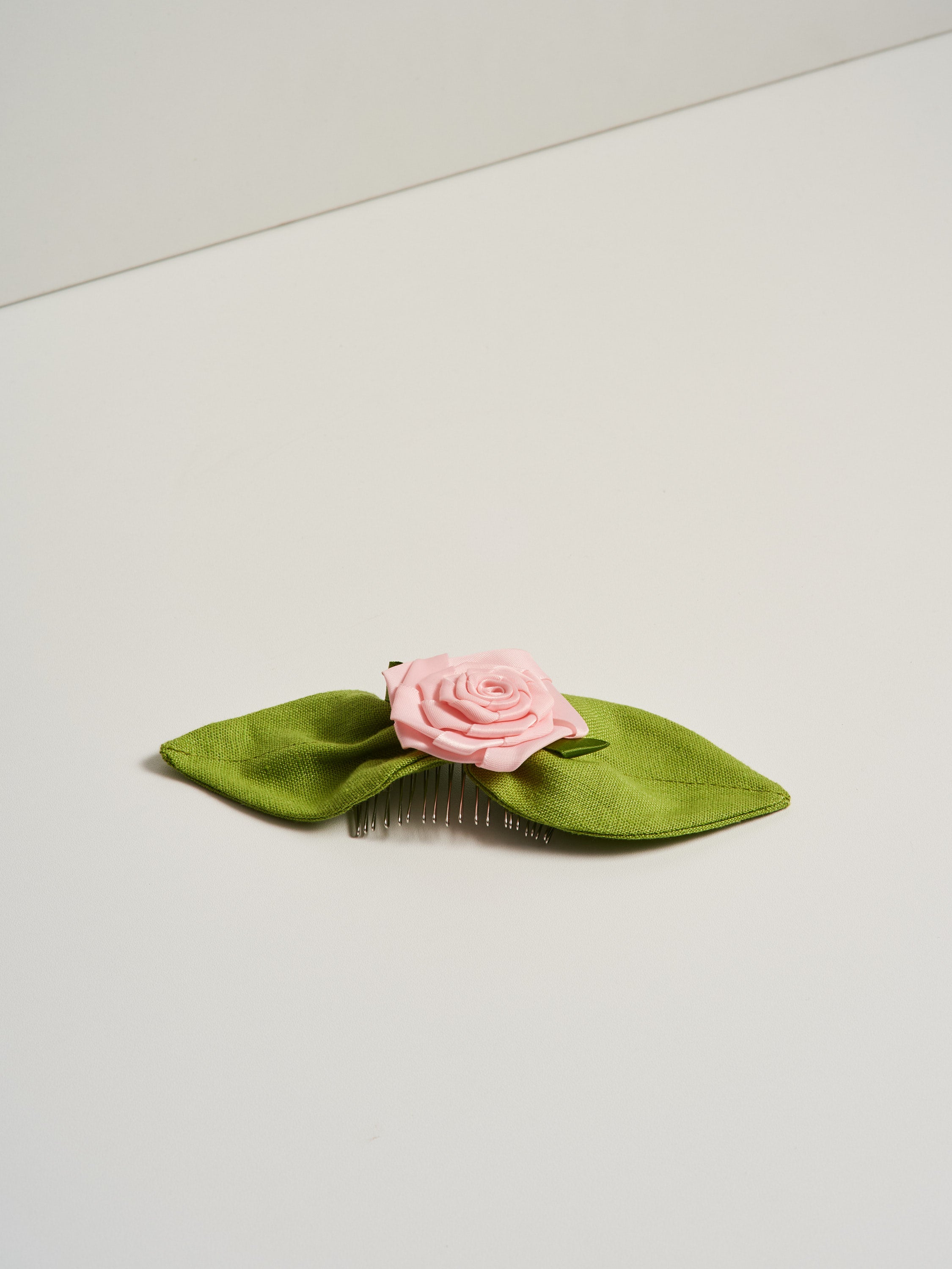 Rosetta hair comb featuring a pink satin rosette and green linen leaves, pictured on a white background.