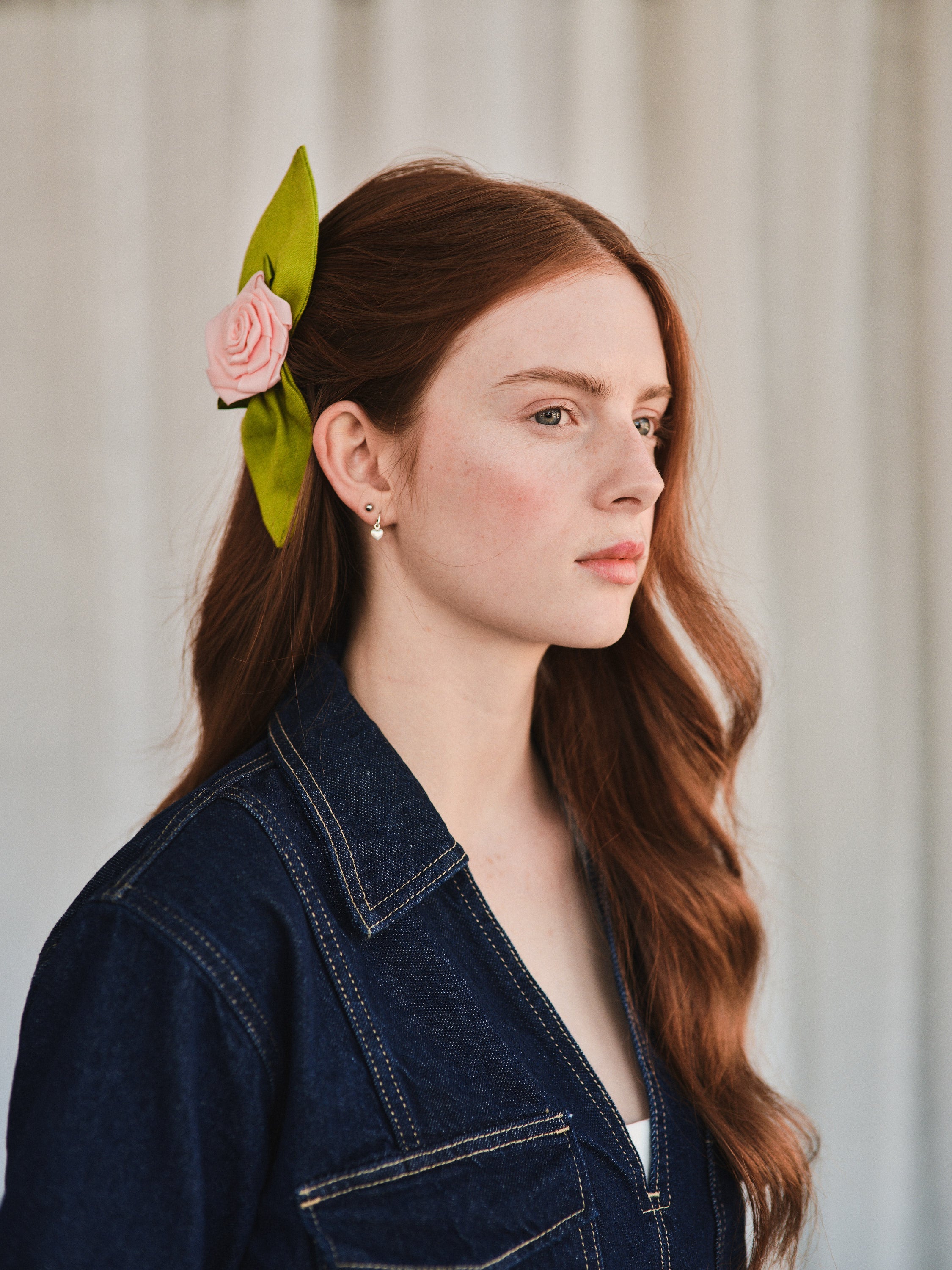 Model with long red hair wears a Rosetta hair comb featuring a pink satin rosette and green linen leaves, styled to the side for a vintage touch.