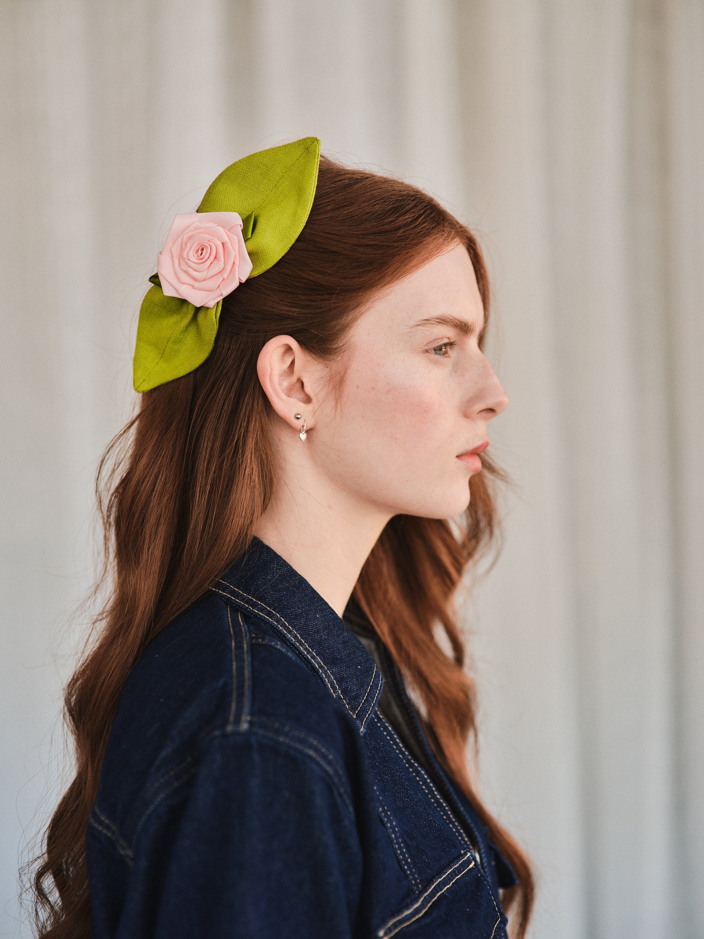 Model with long red hair wears a Rosetta hair comb featuring a pink satin rosette and green linen leaves, styled to the side for a vintage touch.
